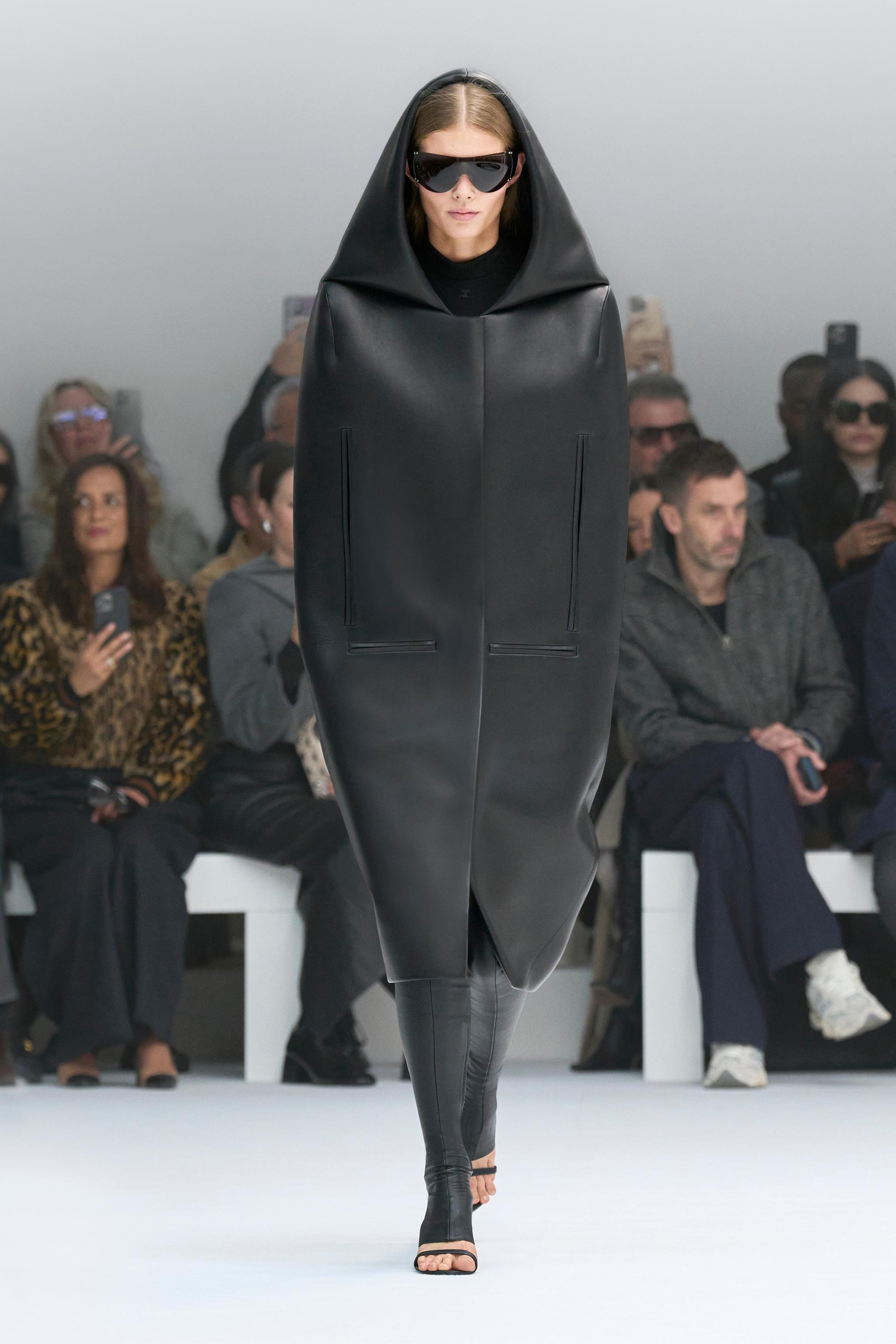 Elegant model in black leather coat and sunglasses walking on a runway for Courrèges.