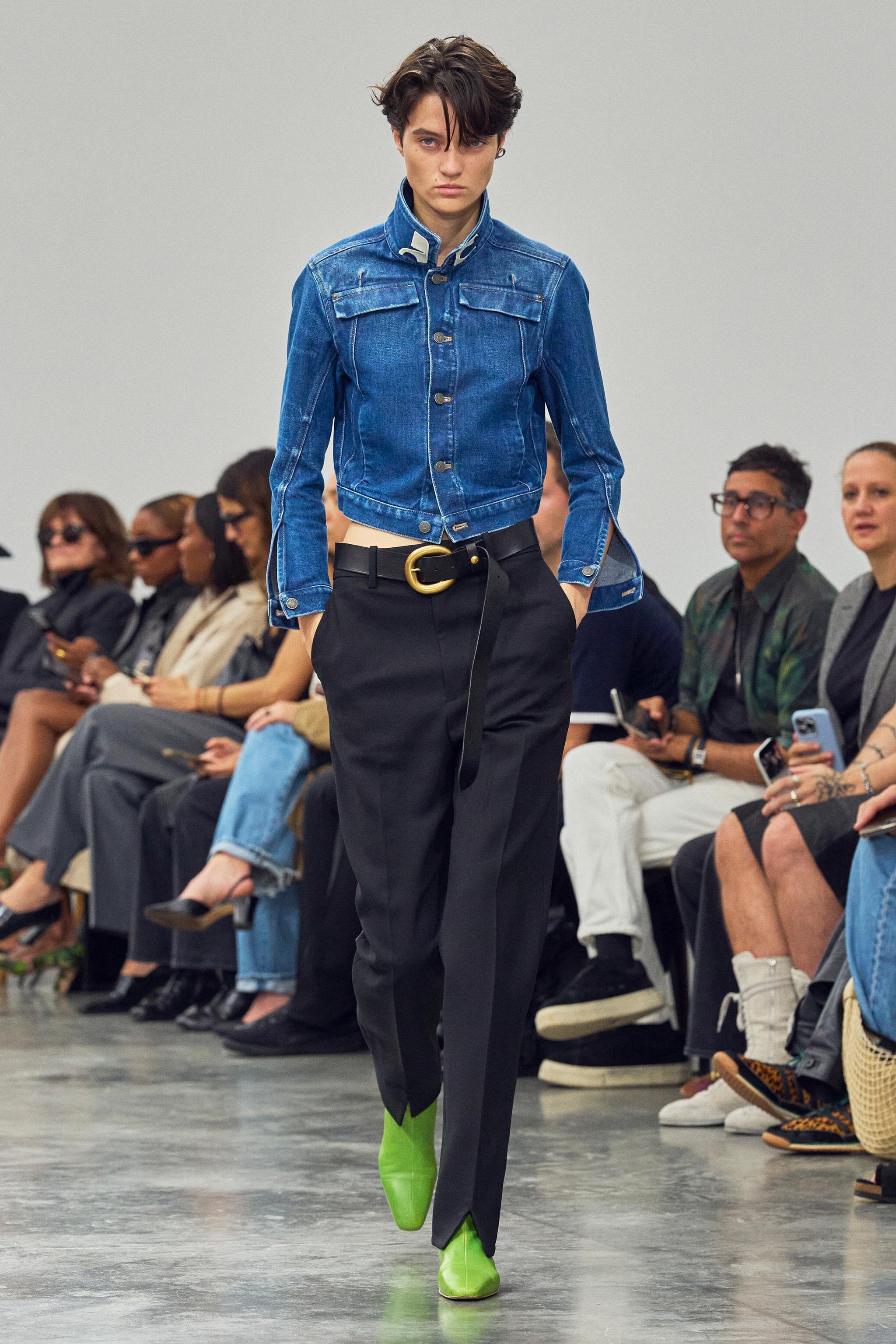 Elegant model walks runway wearing Courrèges denim jacket and high-fashion black trousers.
