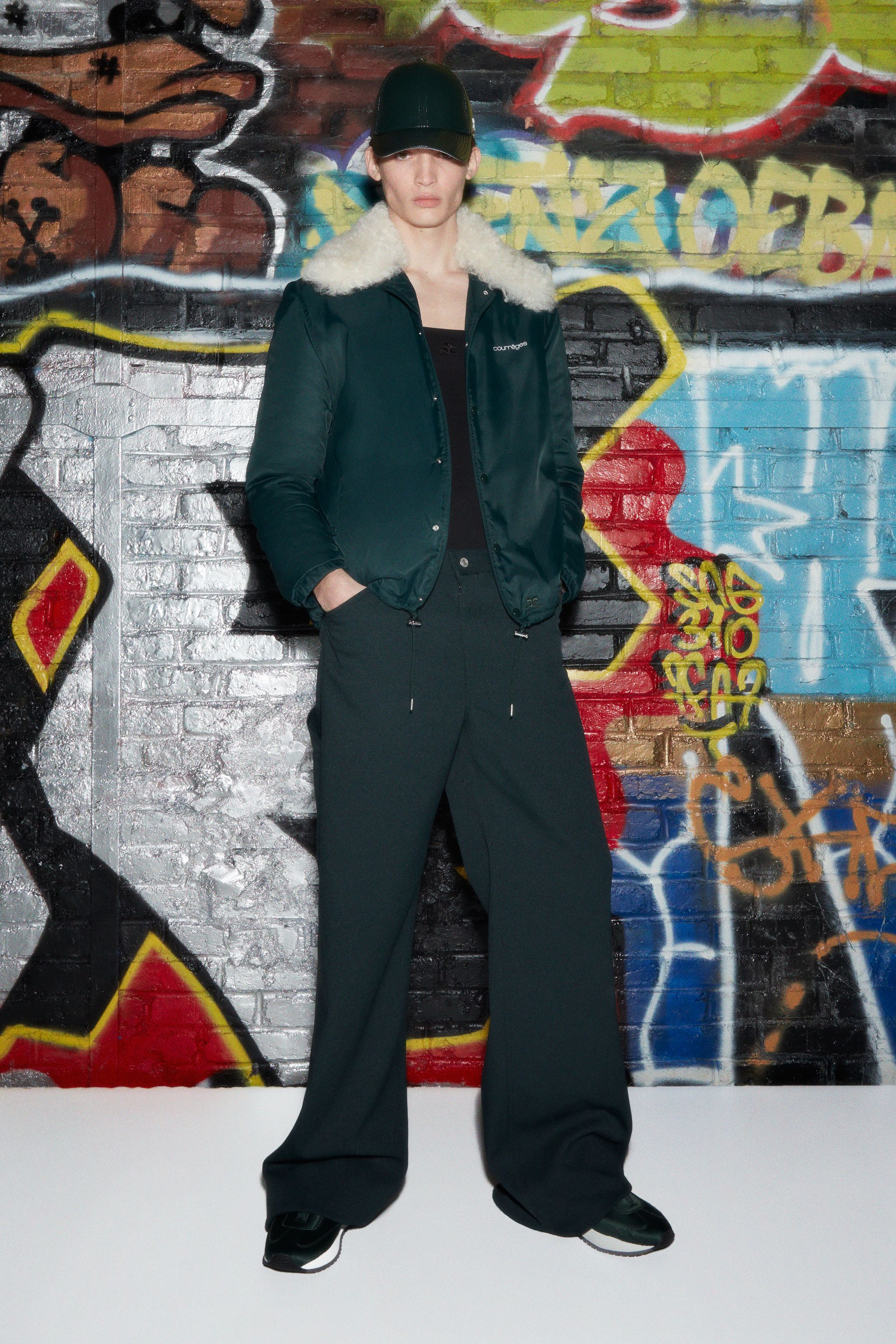 Elegant Courrèges fashion jacket with faux shearling collar, showcased on a model against graffiti.