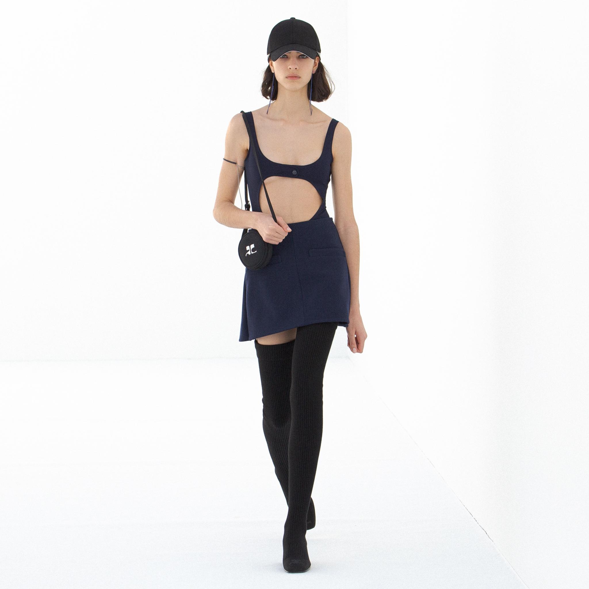 Mode élégante Courrèges avec haut à découpes, jupe bleue et bottes hautes noires.