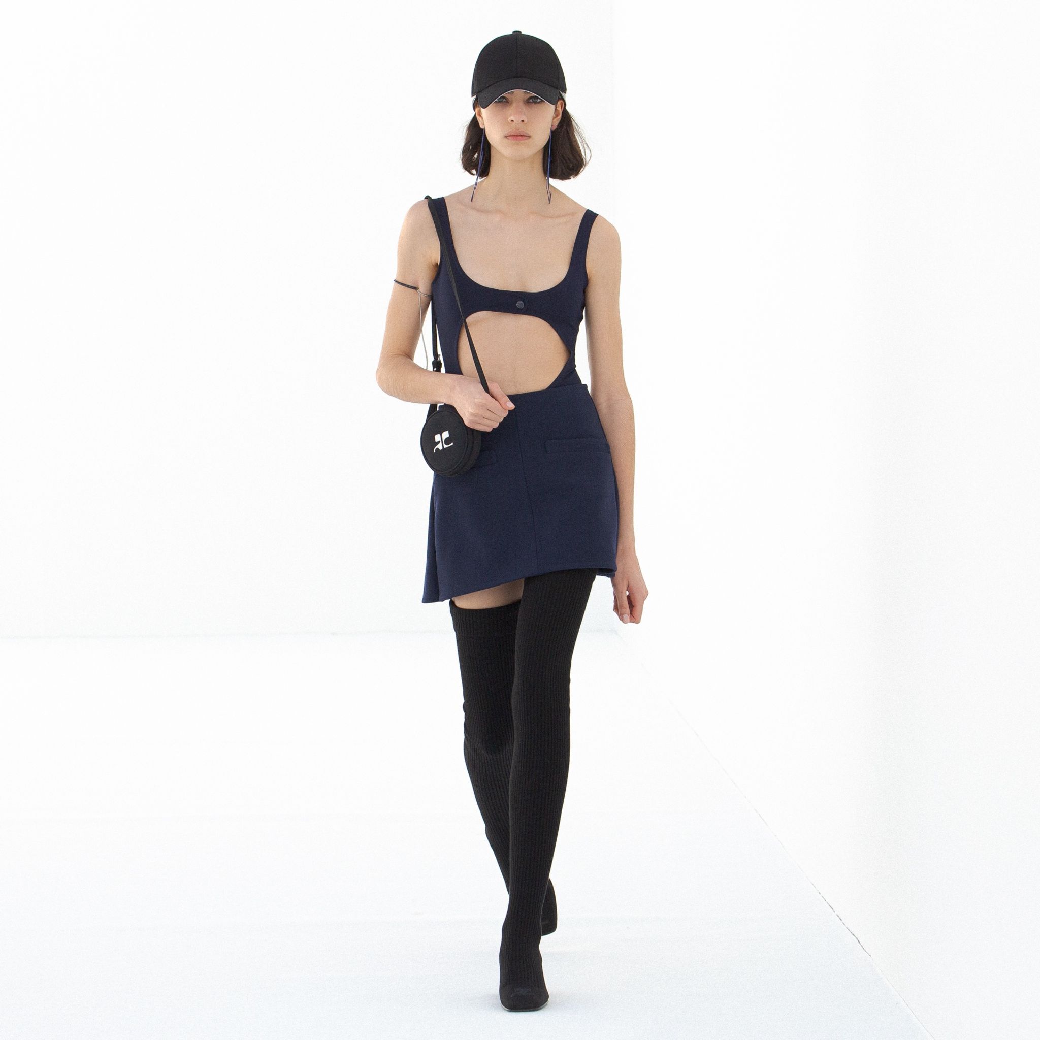 Elegant Courrèges fashion featuring a stylish cutout top, navy skirt, and thigh-high black boots.