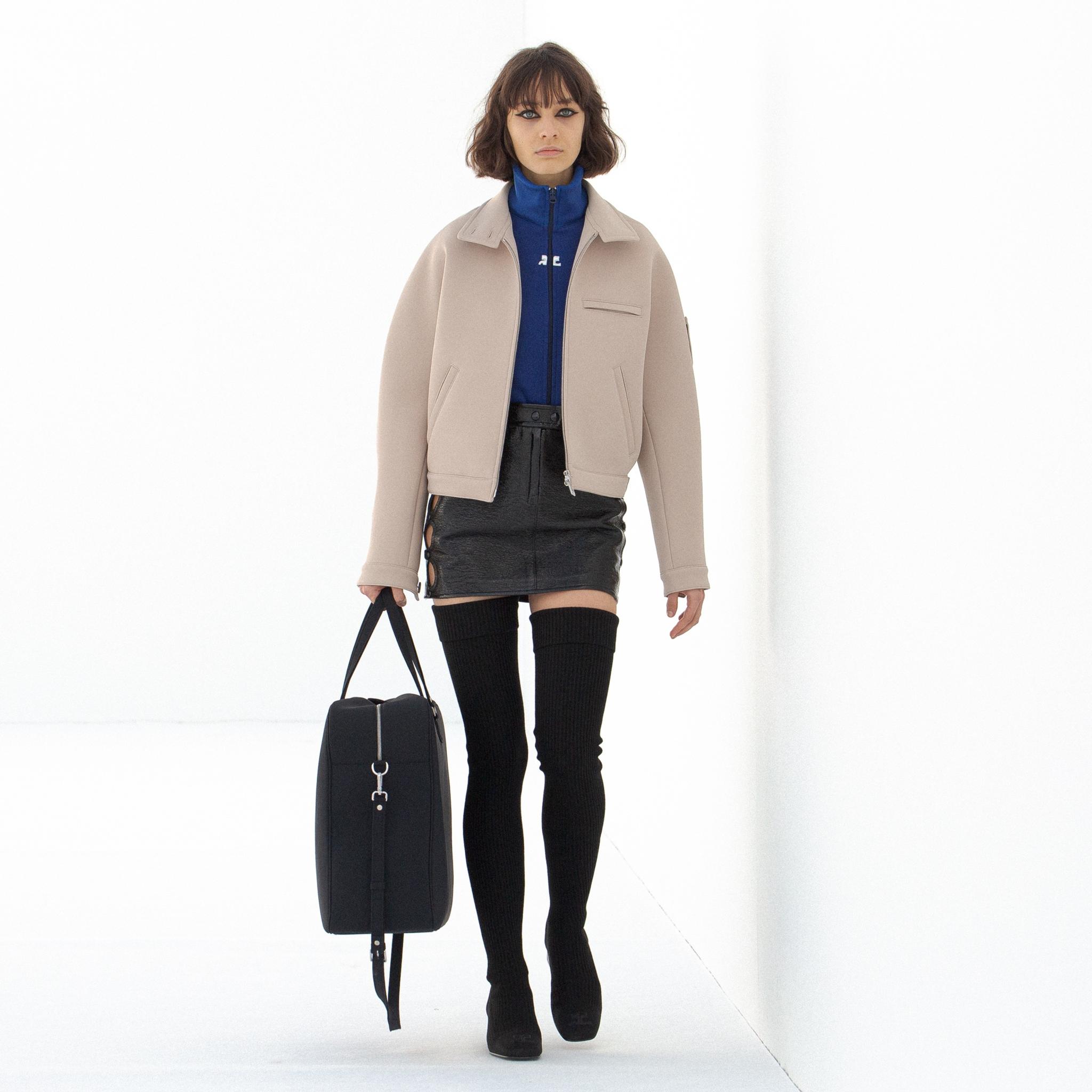 Modèle élégant dans la mode Courrèges, portant une veste beige, haut bleu, mini-jupe noire et chaussettes hautes.