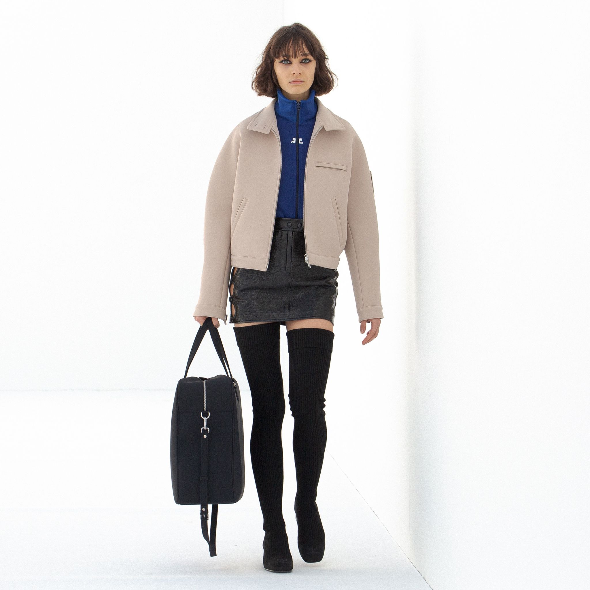 Elegant model in Courrèges fashion, wearing a beige jacket, blue top, black mini skirt, and thigh-high socks.
