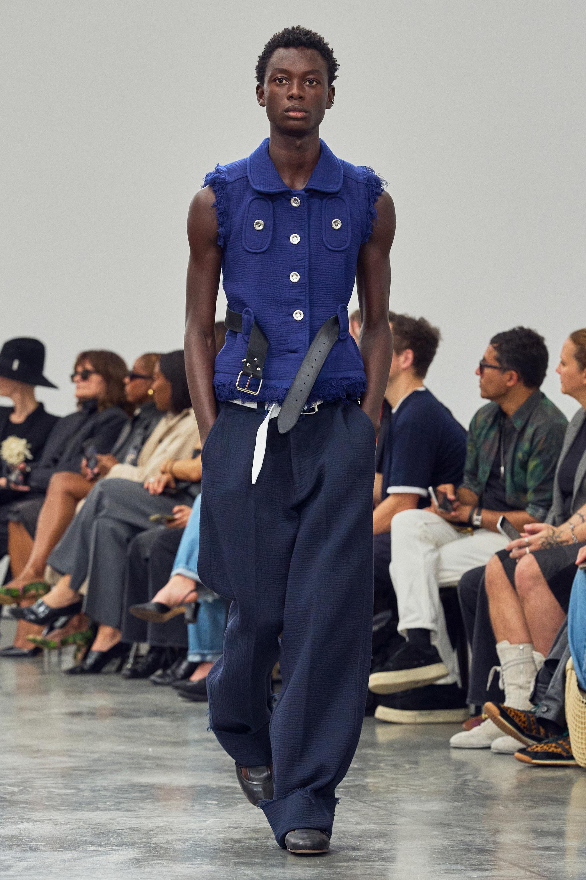 Fashion runway model showcasing avant-garde blue top and loose dark trousers for Courrèges.