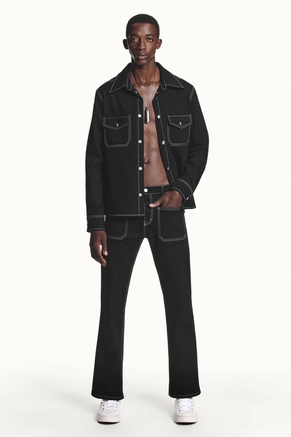 Elegant black denim jacket and jeans set with contrasting white stitching, on a fashion model.