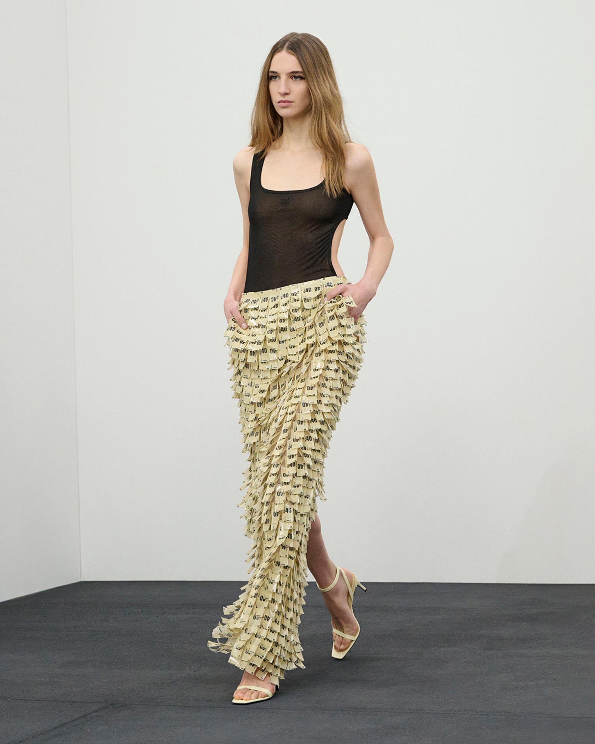 Fashion model wearing a black top and ruffled beige pants with printed labels, on Courrèges website.