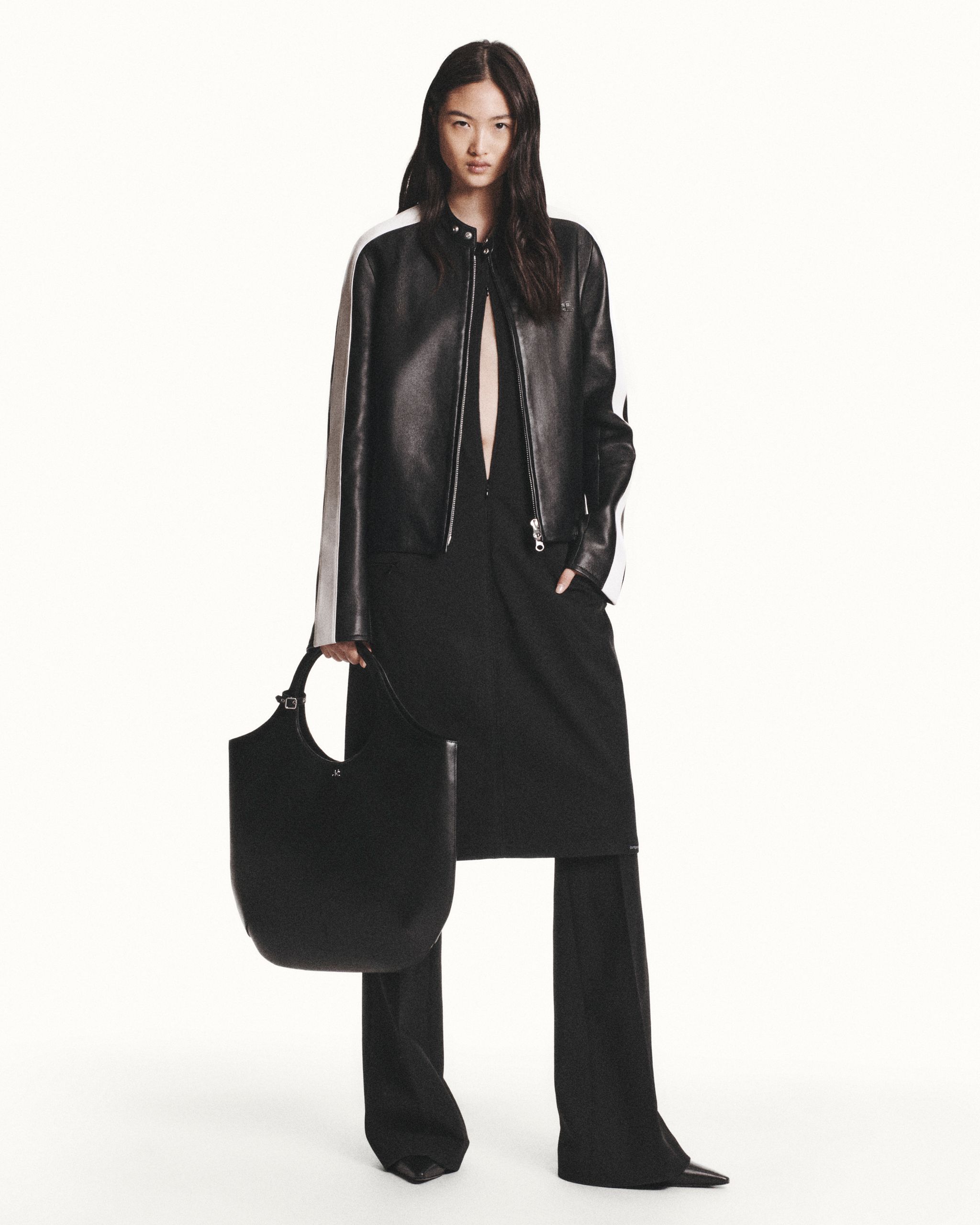 Elegant woman in black leather jacket and wide-leg pants, holding a stylish black bag for Courrèges.