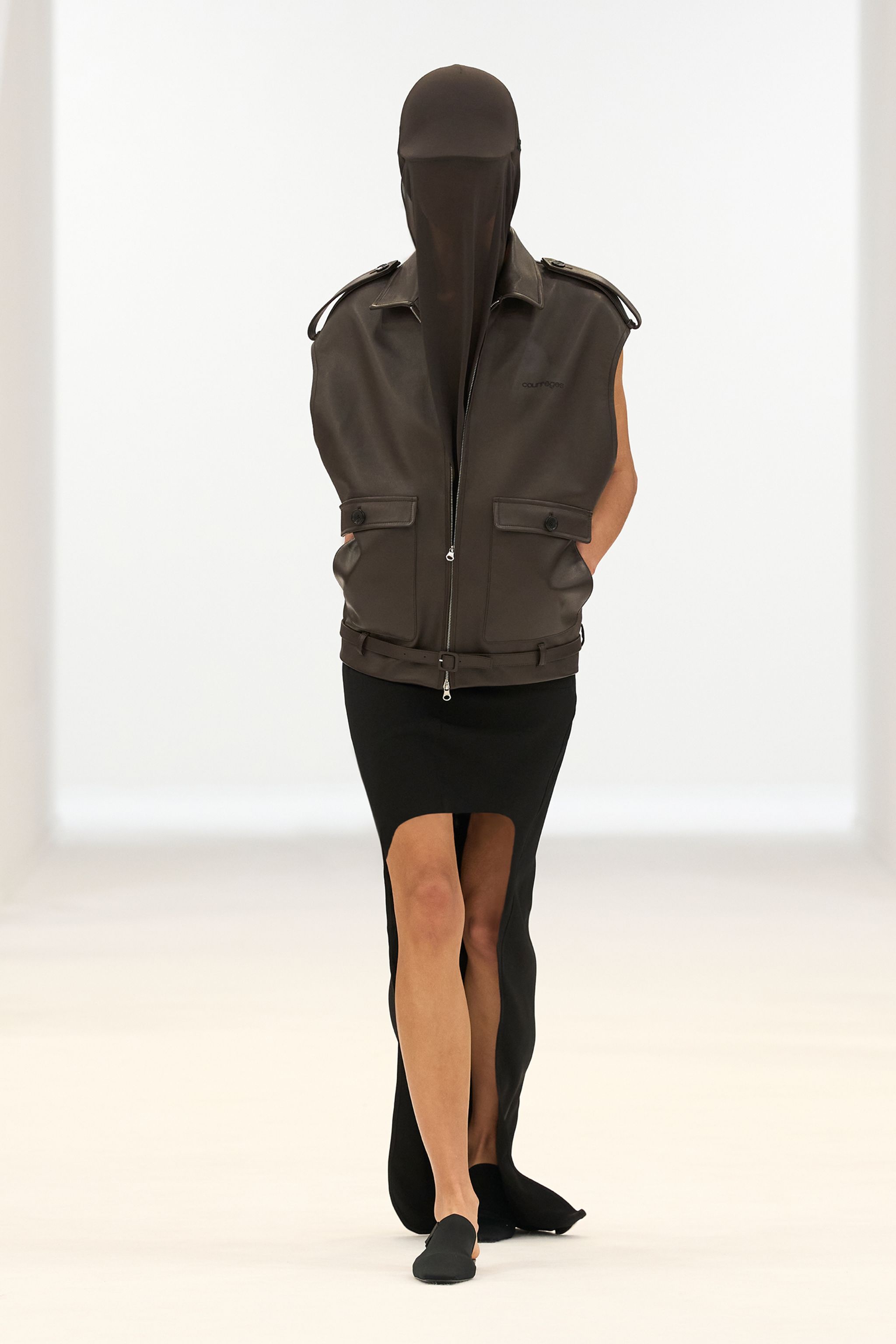 Elegant black sleeveless dress with a high slit, styled with a brown leather vest for Courrèges.