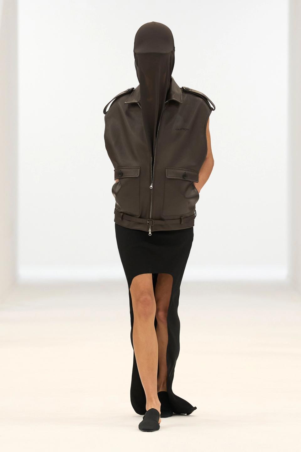 Elegant black sleeveless dress with a high slit, styled with a brown leather vest for Courrèges.