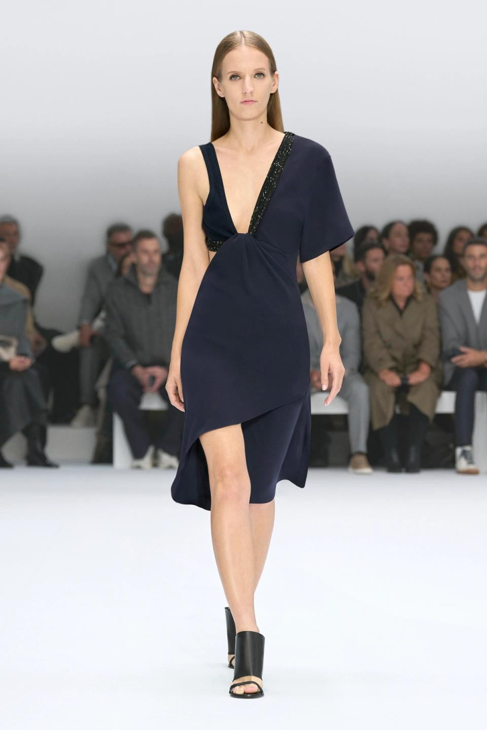 Elegant navy blue dress with asymmetric design, showcased on a runway for Courrèges.