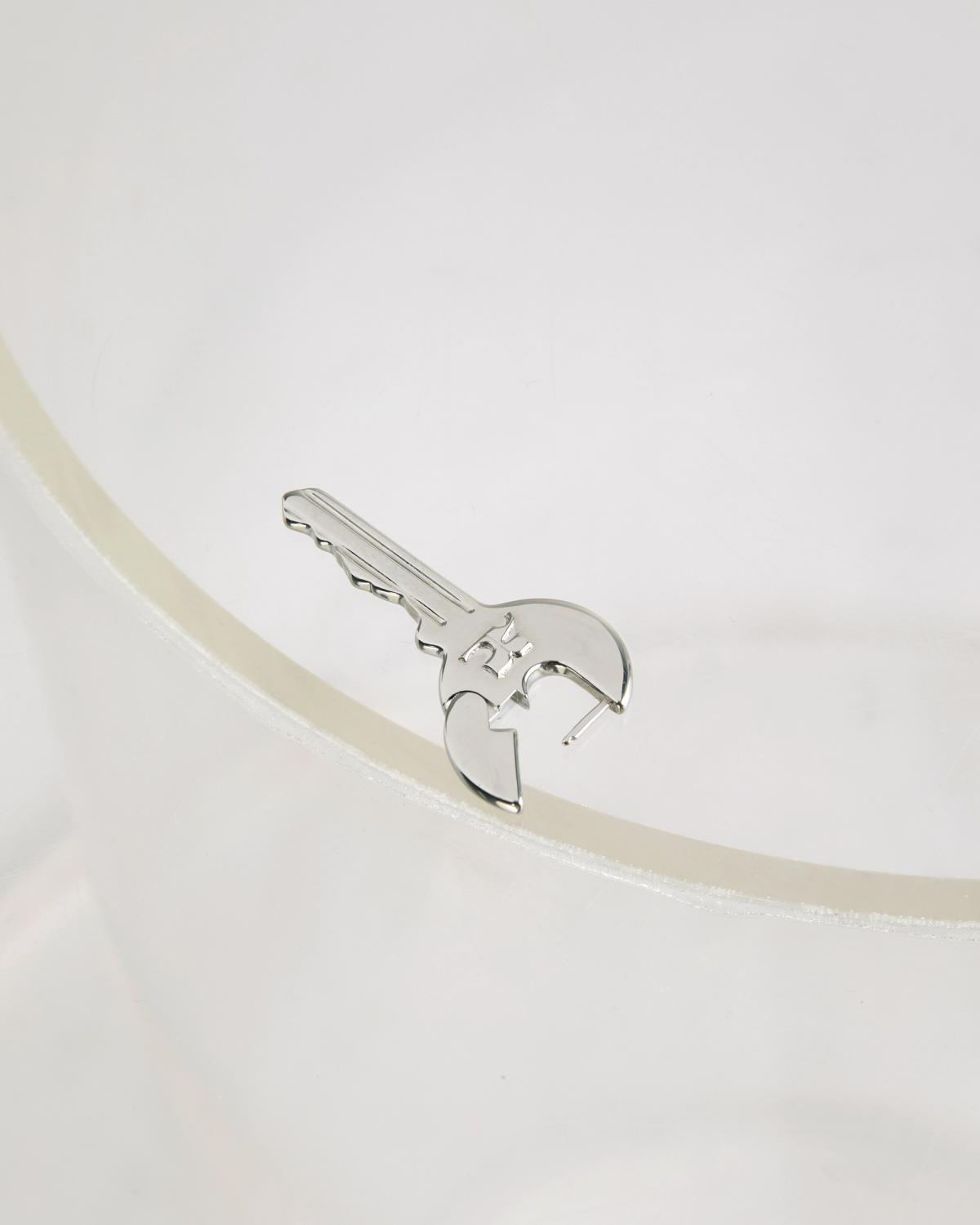 Close-up of a polished silver Courrèges key-shaped charm resting on a soft white surface.