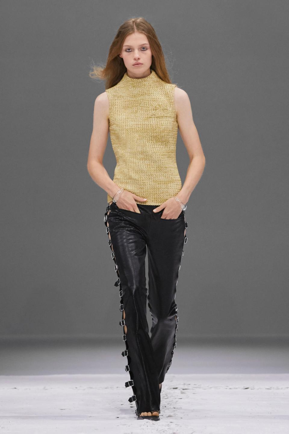 Elegant model wearing a sleeveless yellow top and black pants with side buckle details, Courrèges.