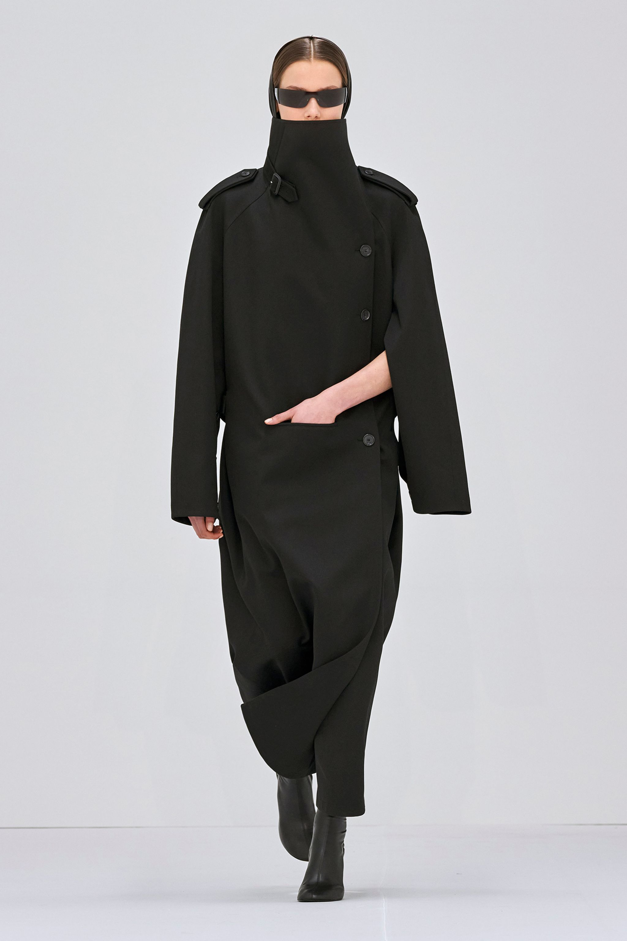 Elegant black trench coat with high collar, designed for Courrèges fashion, on a runway model.