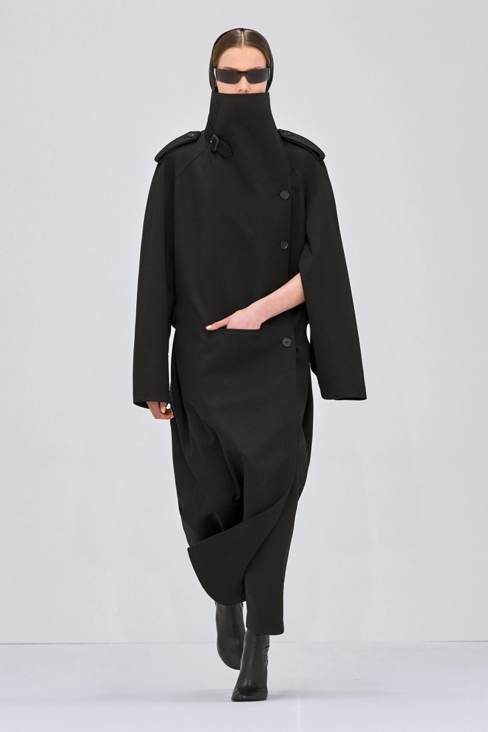 Elegant black trench coat with high collar, designed for Courrèges fashion, on a runway model.