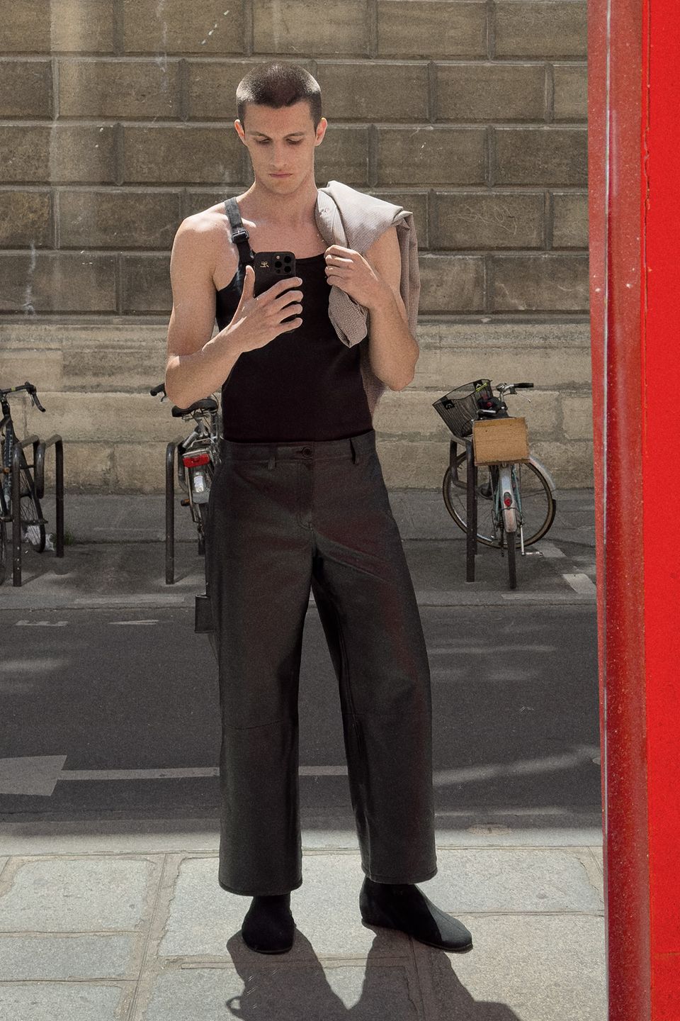 Elegant Courrèges fashion photo of a model in black outfit taking a mirror selfie outdoors.
