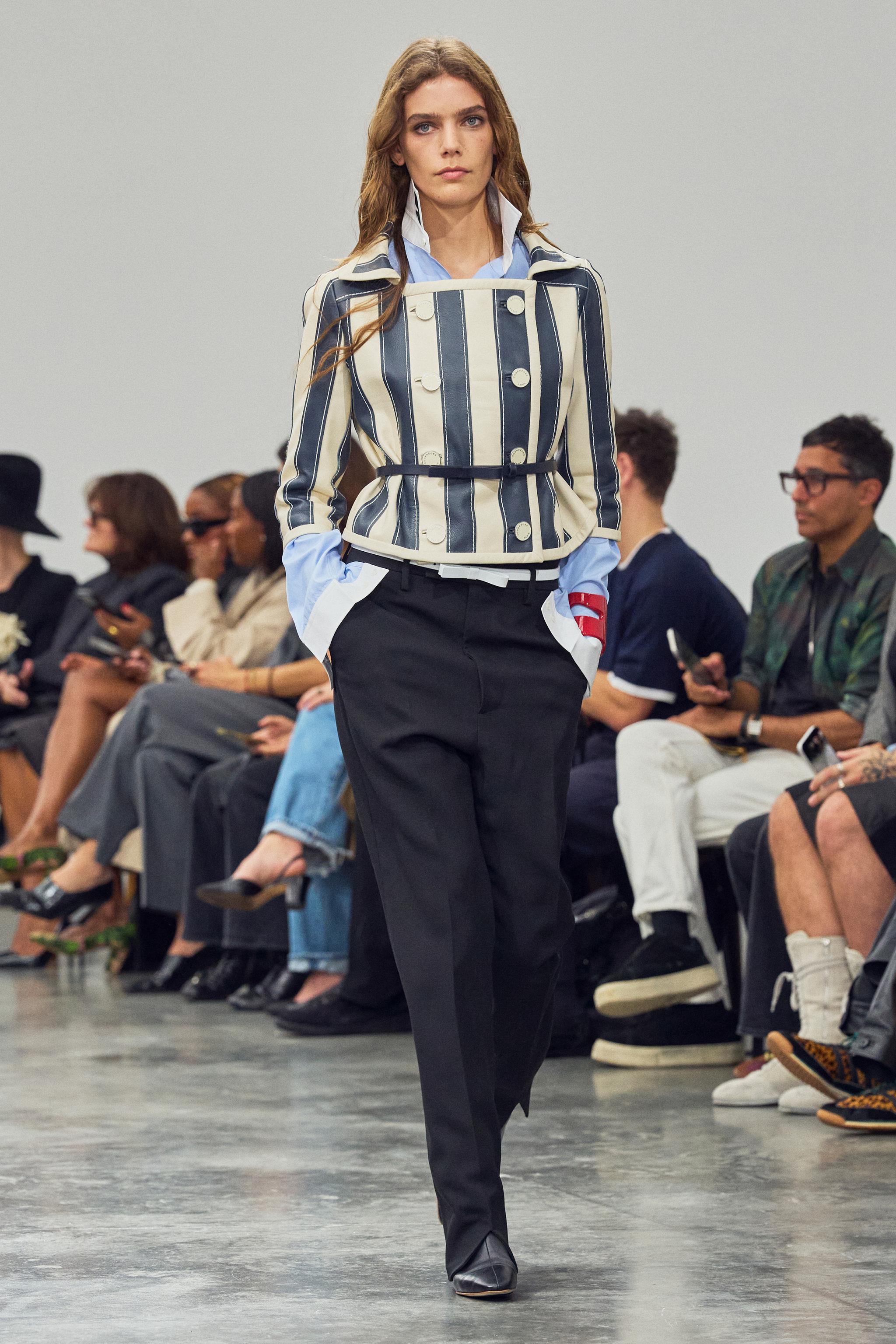 Fashionable model walking runway wearing Courrèges stylish striped jacket at a fashion show.