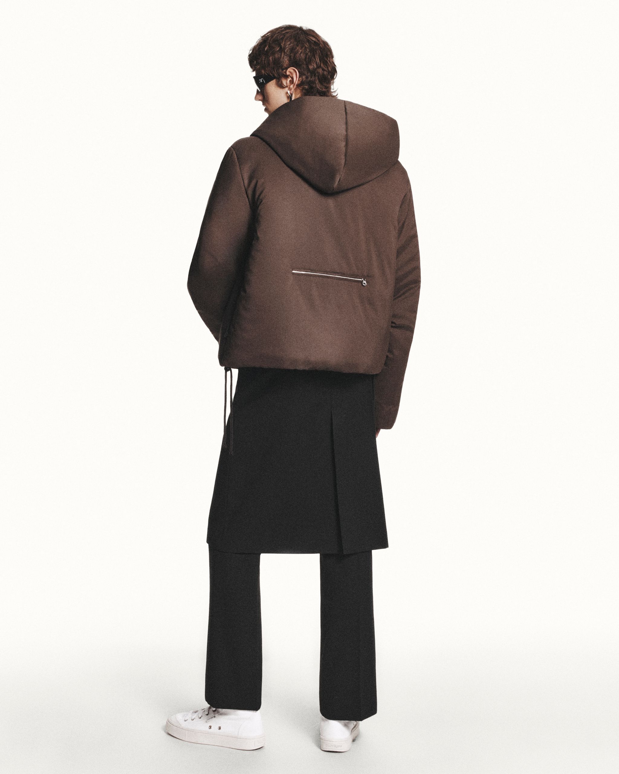 Model wearing a brown hooded puffer jacket, black skirt, and white sneakers for Courrèges.