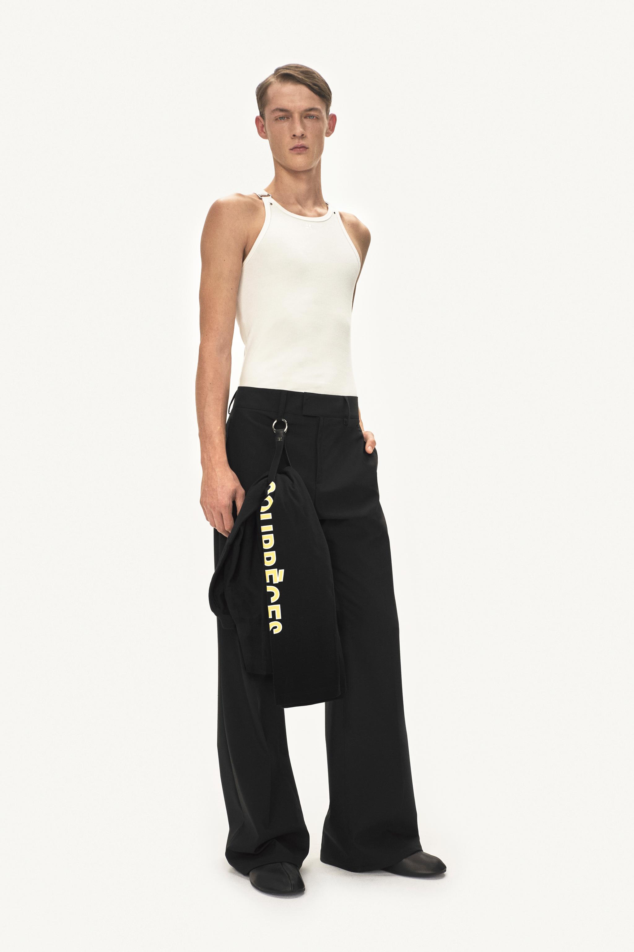 Modèle élégant portant une tenue Courrèges, top sans manches blanc et pantalon large noir.