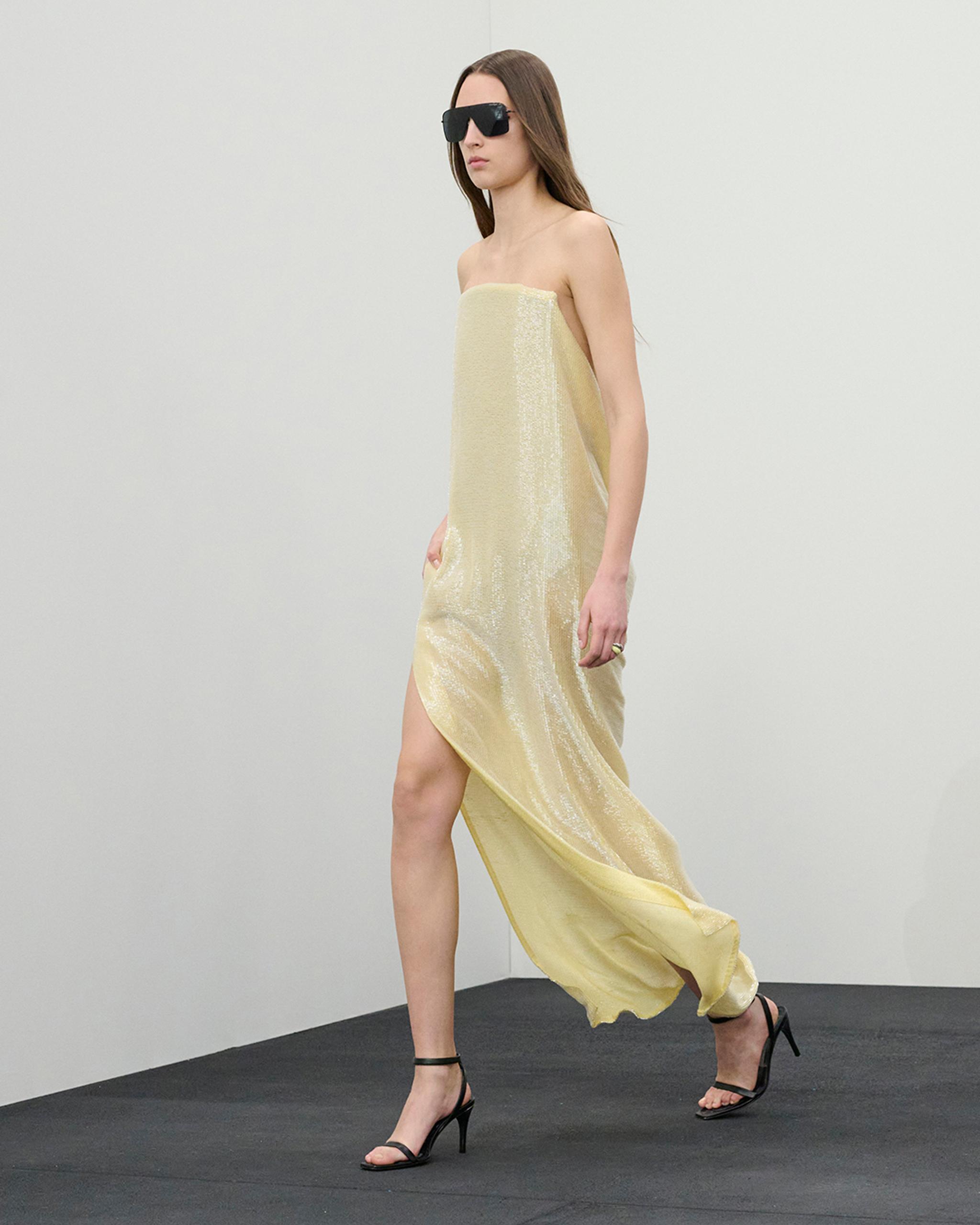 Elegant gold strapless dress with high slit, accessorized with black sunglasses and heels.