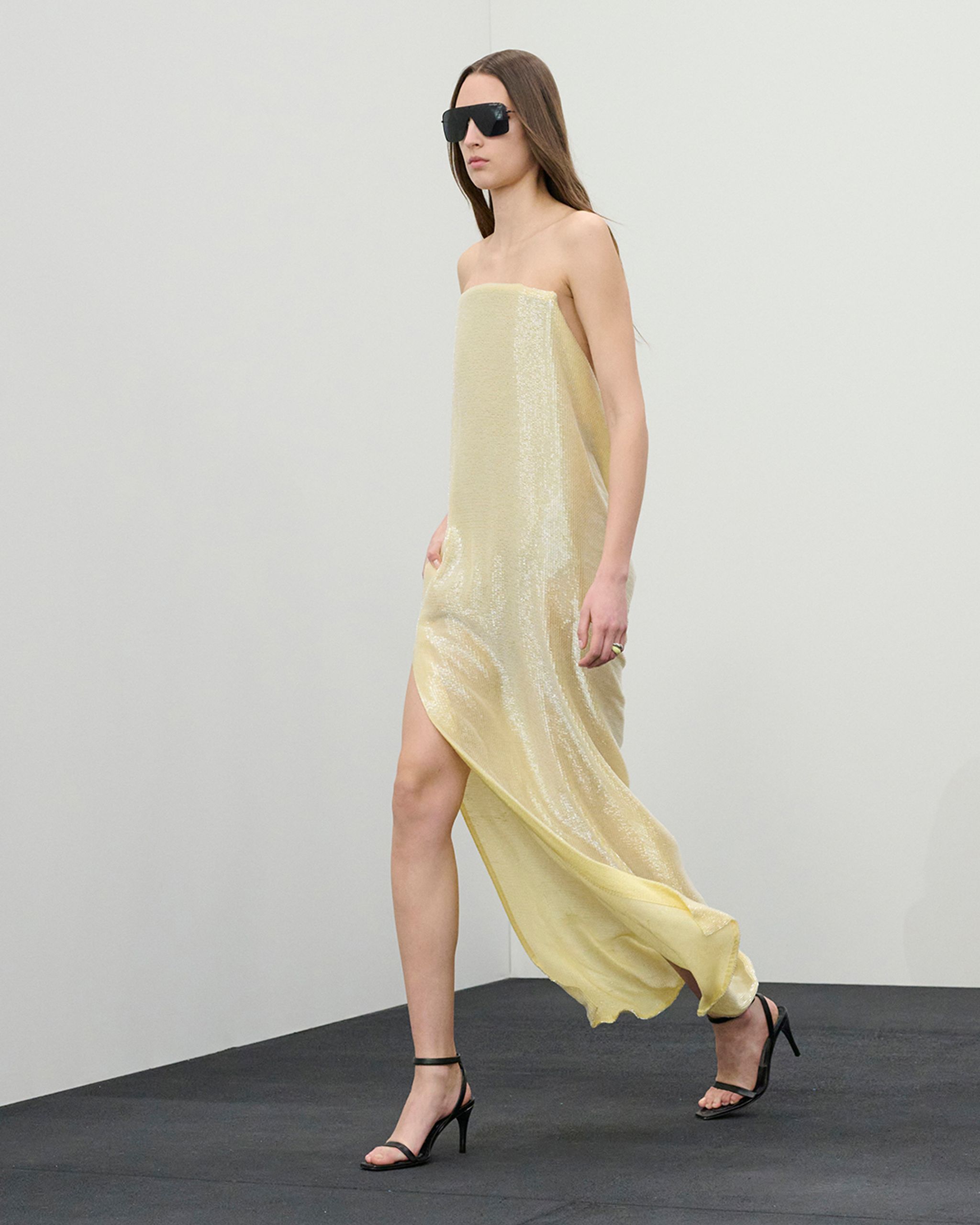 Robe dorée sans bretelles avec fente haute, accessoirisée de lunettes noires et talons. 