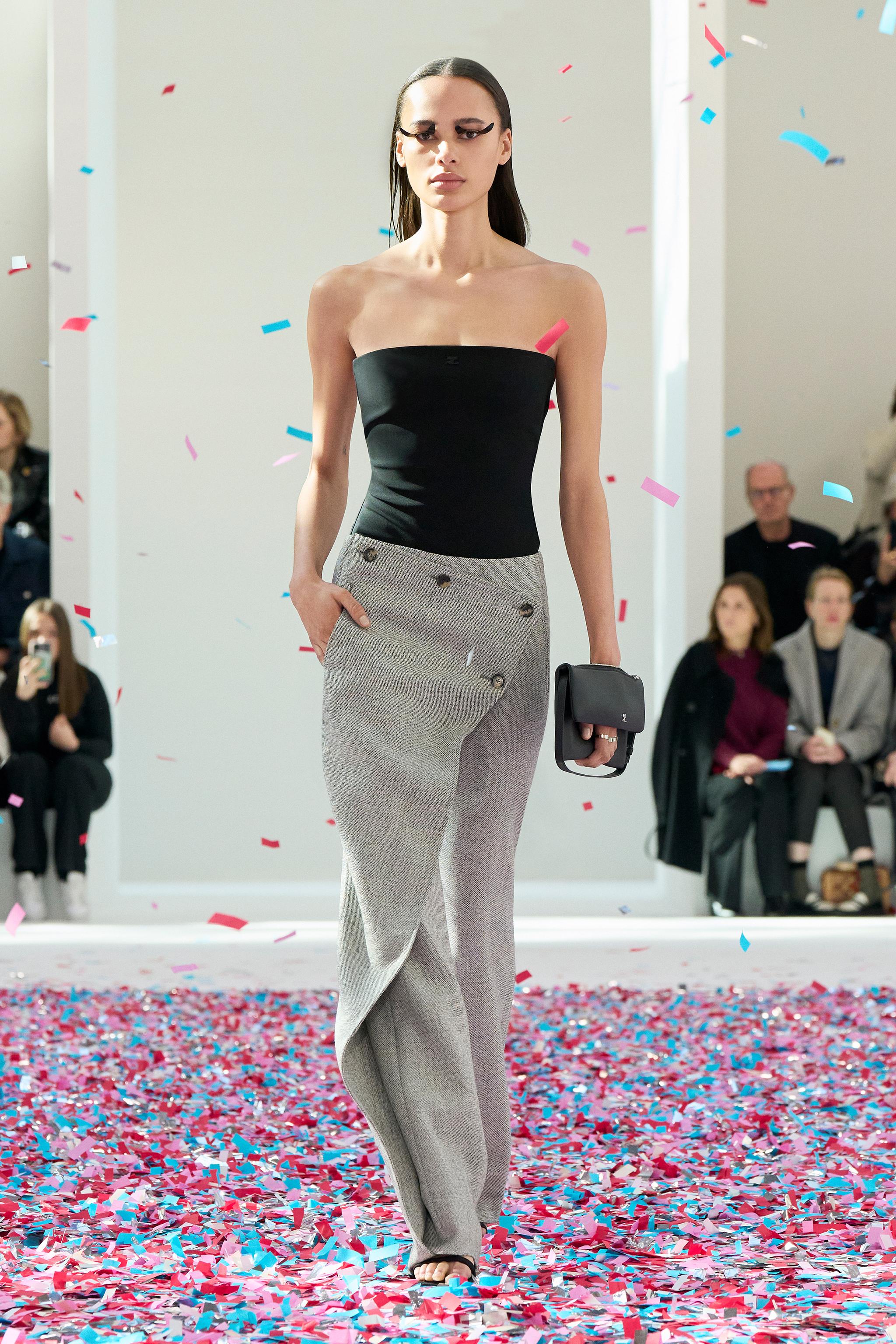 Elegant female model walking runway in black top and gray trousers during Courrèges fashion show.