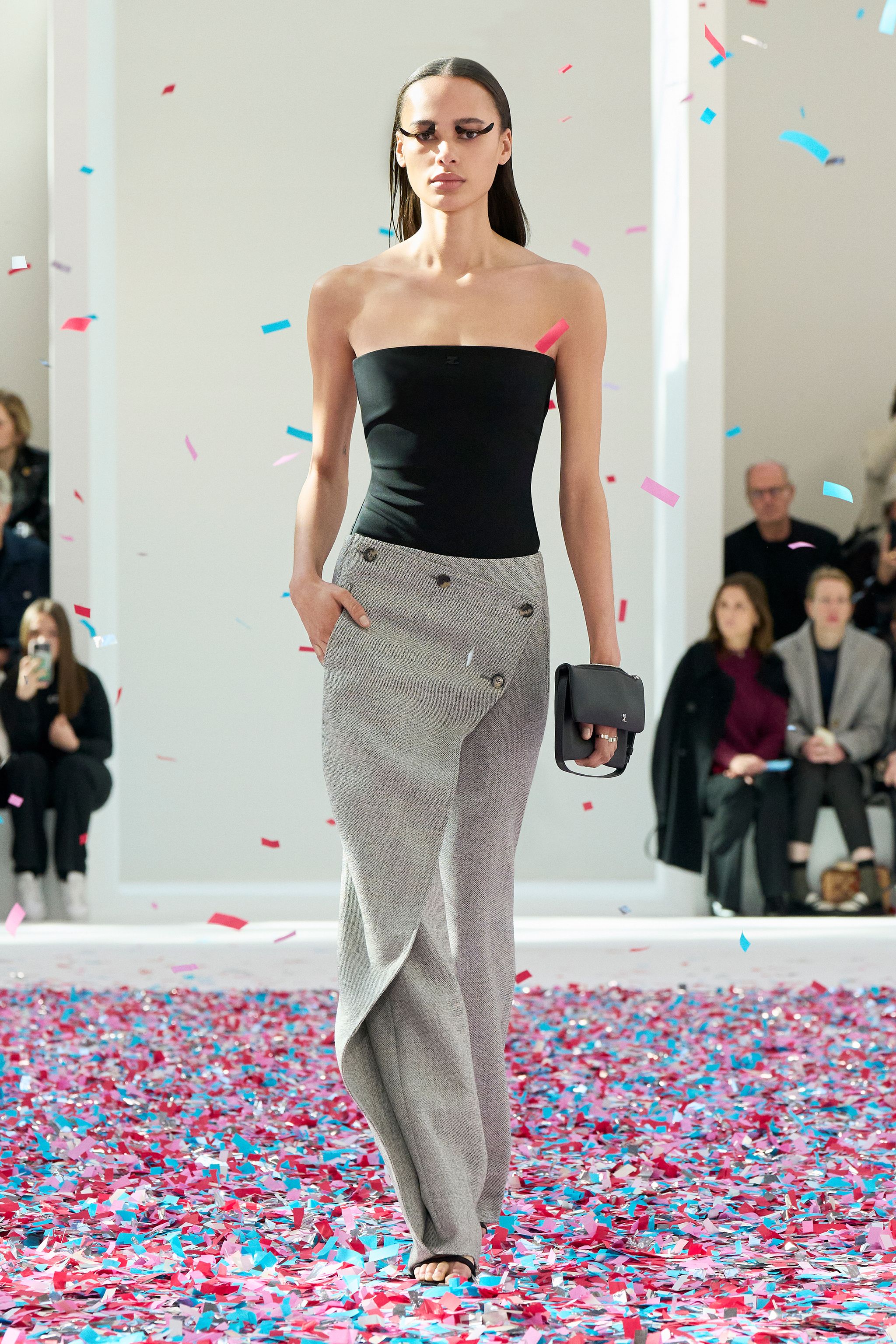 Elegant model in black top and gray trousers walking on a colorful confetti runway for Courrèges.