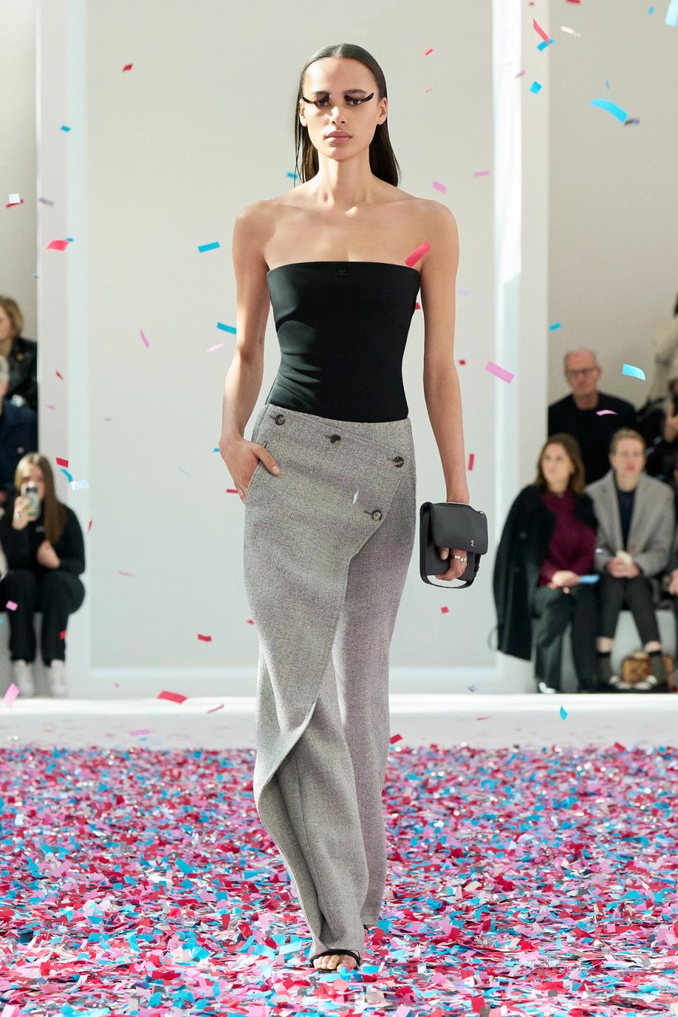 Elegant model in black top and gray trousers walking on a colorful confetti runway for Courrèges.