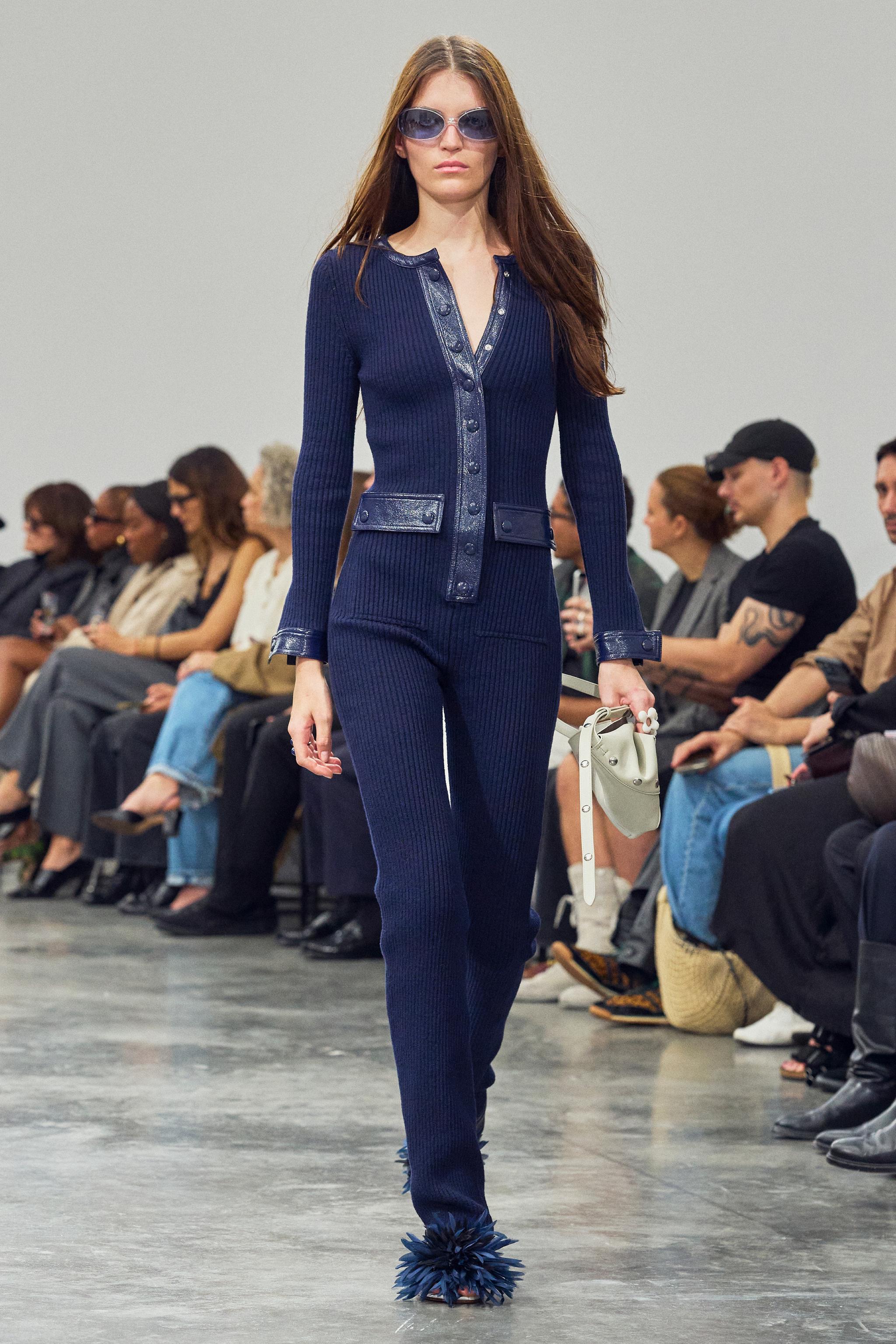 Elegant model showcasing Courrèges' chic navy blue knitted jumpsuit on runway.