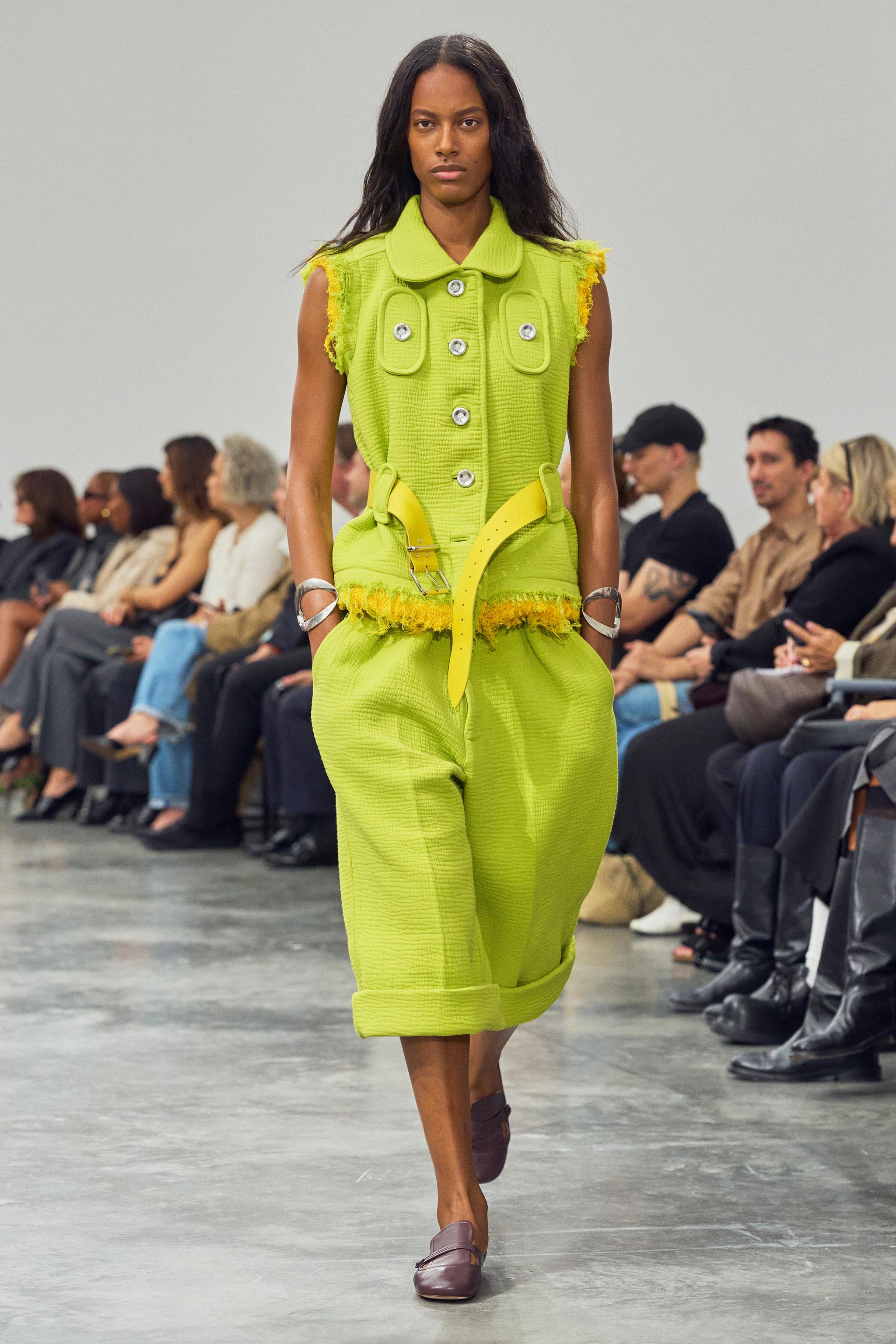 Elegant lime green fashion vest and pants by Courrèges on runway, with seated audience.