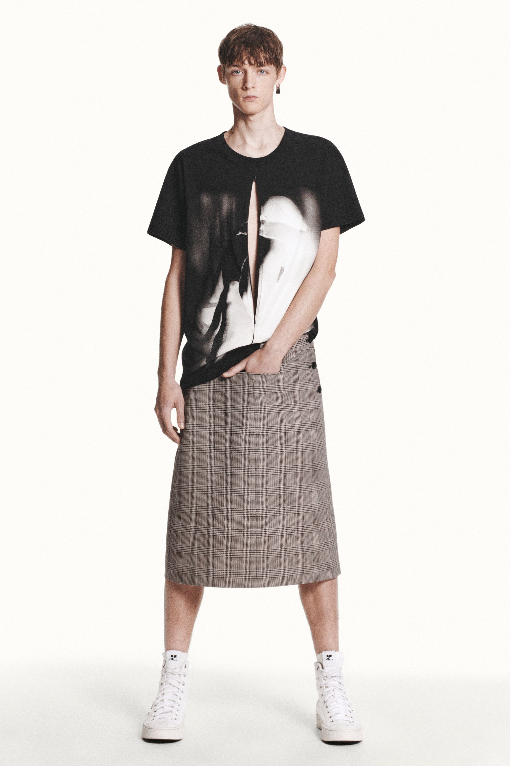 Elegant Courrèges fashion display featuring a model in a graphic zip-up T-shirt, plaid skirt, and white sneakers.