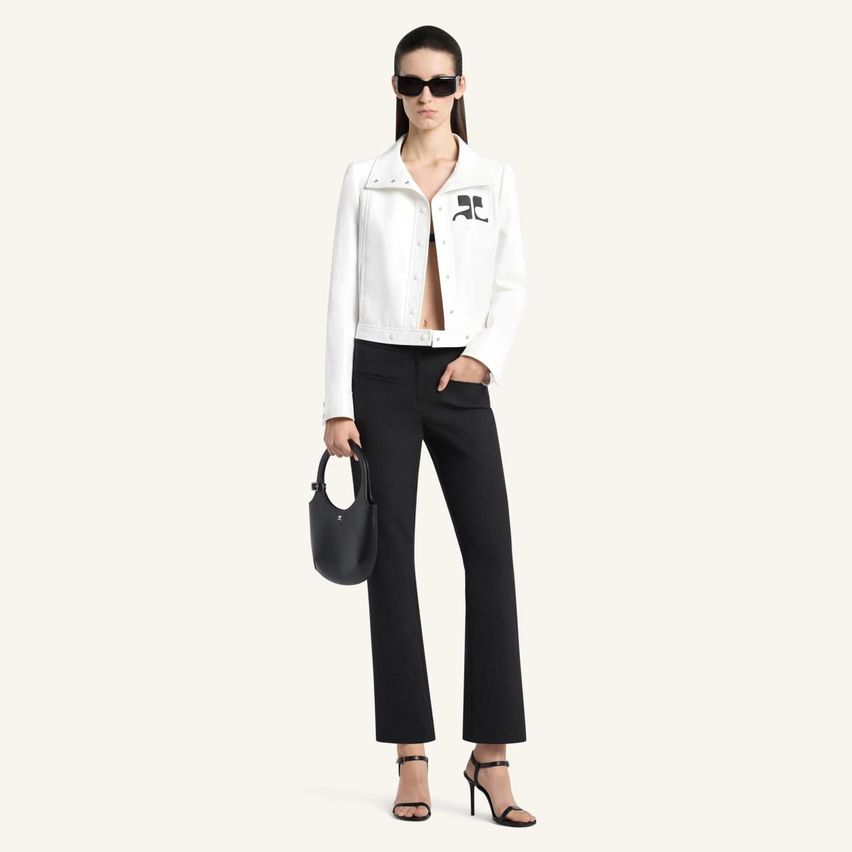 Elegant woman in black pants, white jacket, sunglasses, and heels, showcasing Courrèges fashion.