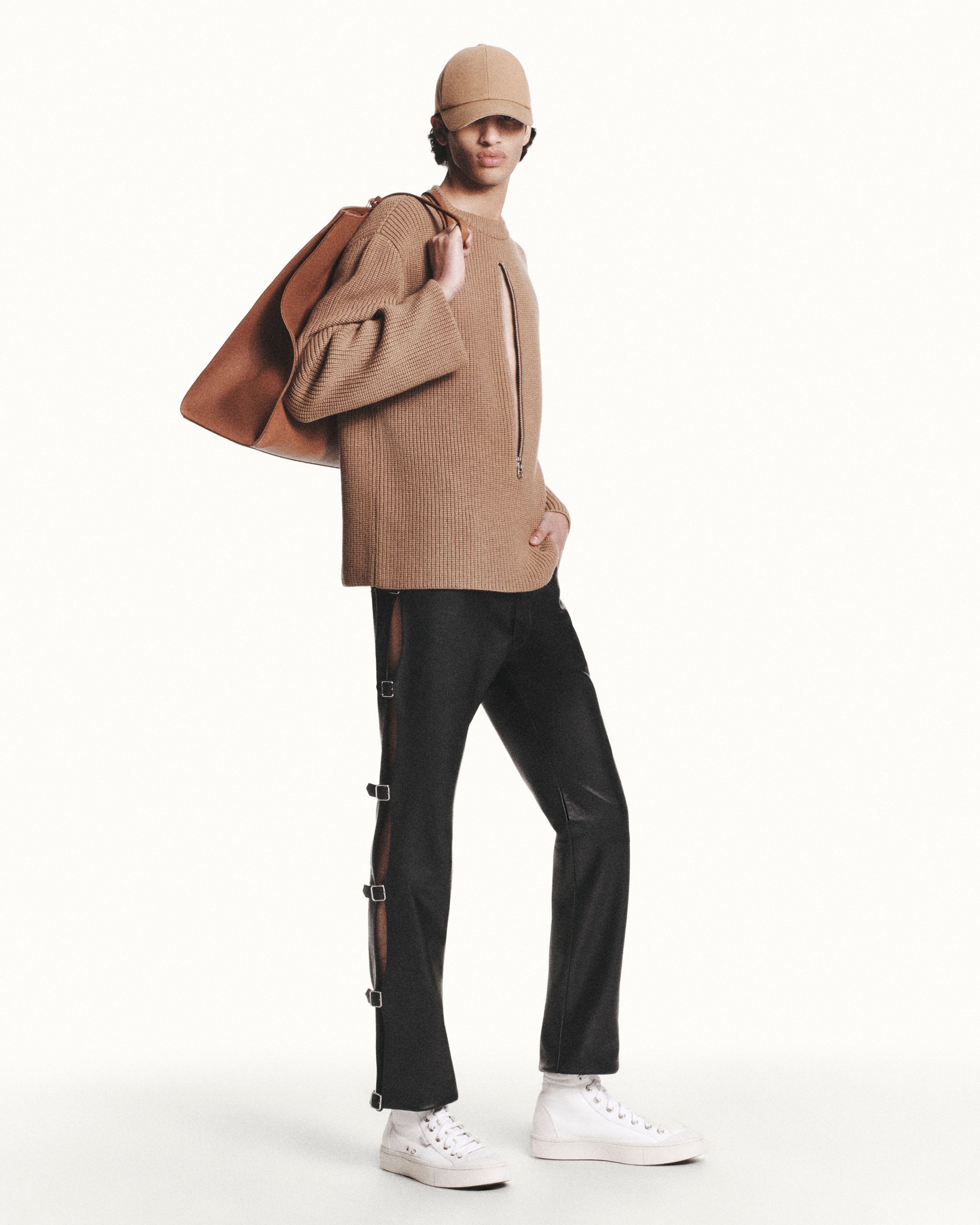 Elegant Courrèges fashion model showcasing a stylish brown sweater, cap, casual trousers, and sneakers.