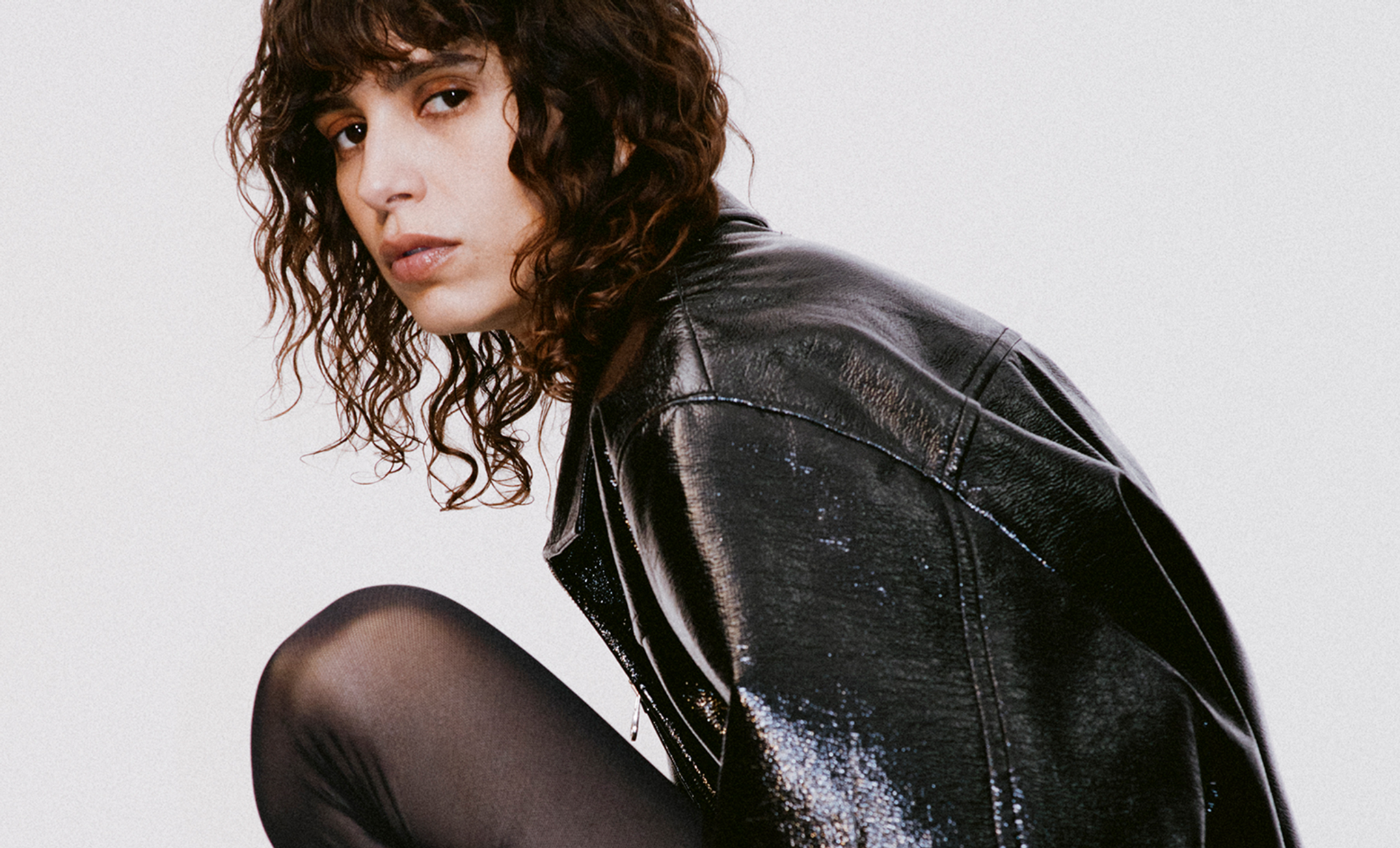 Elegant model in black leather jacket and tights, showcasing Courrèges fashion on an ecommerce site.