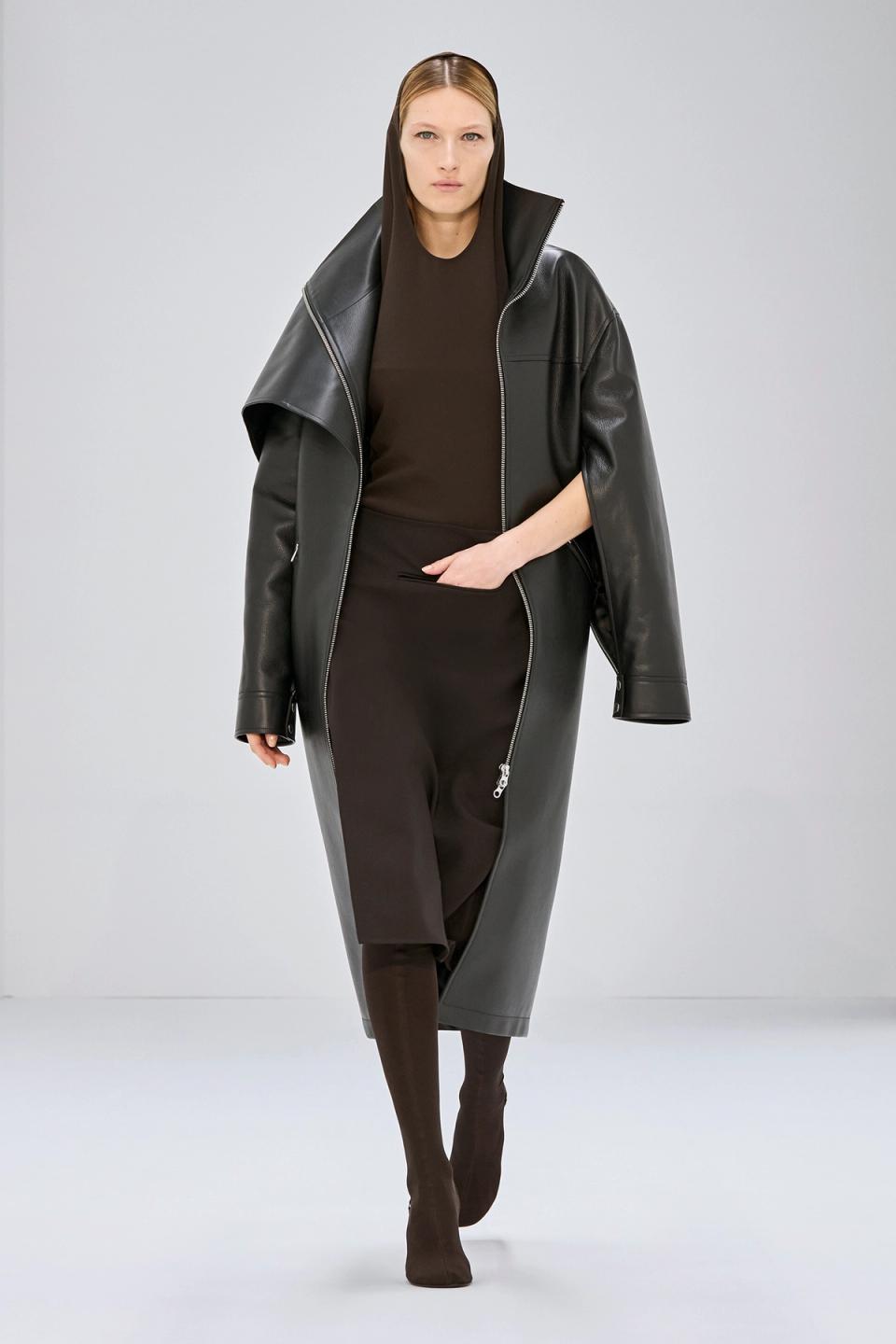 Elegant black leather coat by Courrèges featuring a modern oversized hood on a runway model.