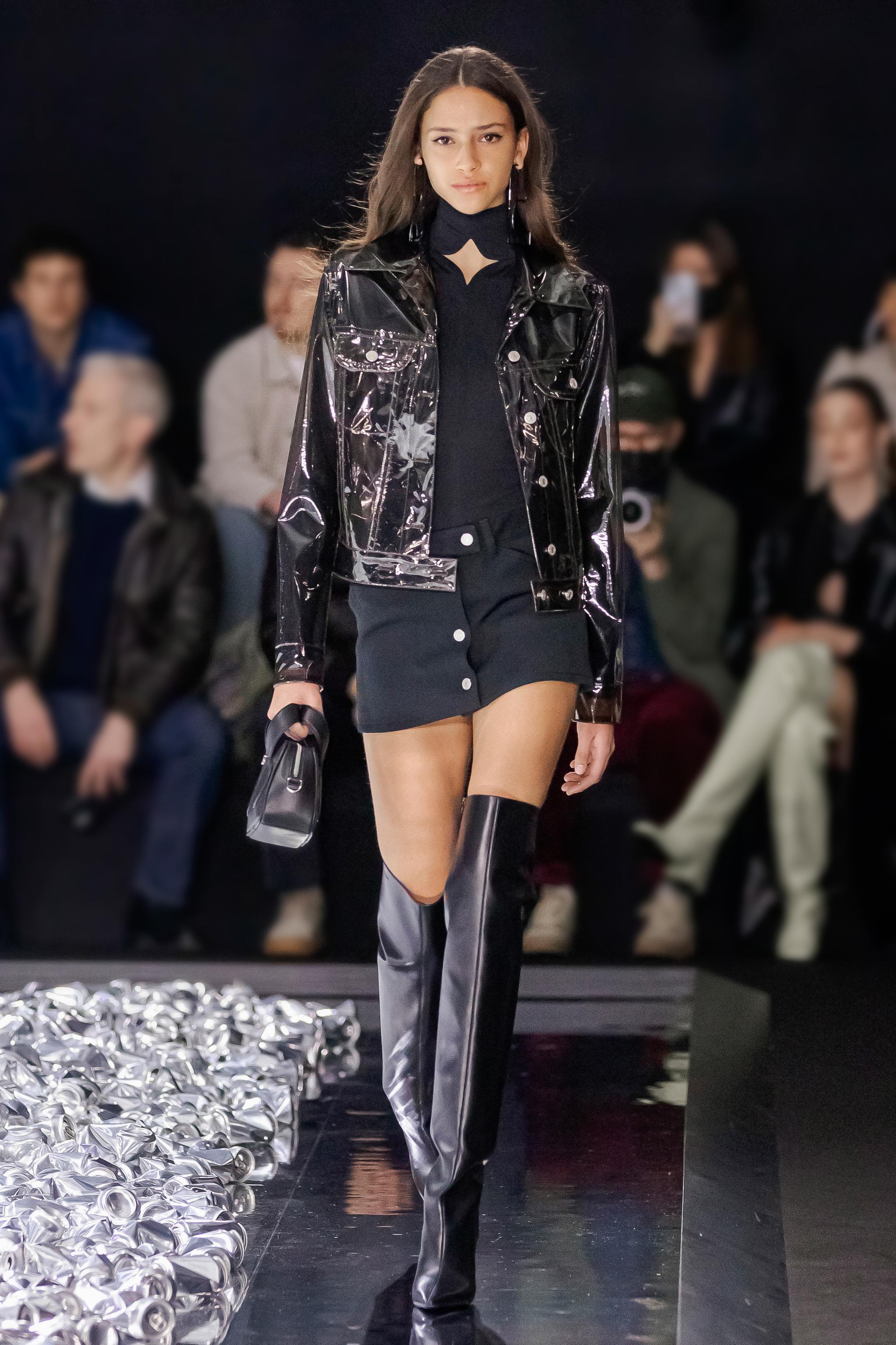 Elegant model walking runway in black Courrèges outfit with shiny thigh-high boots.
