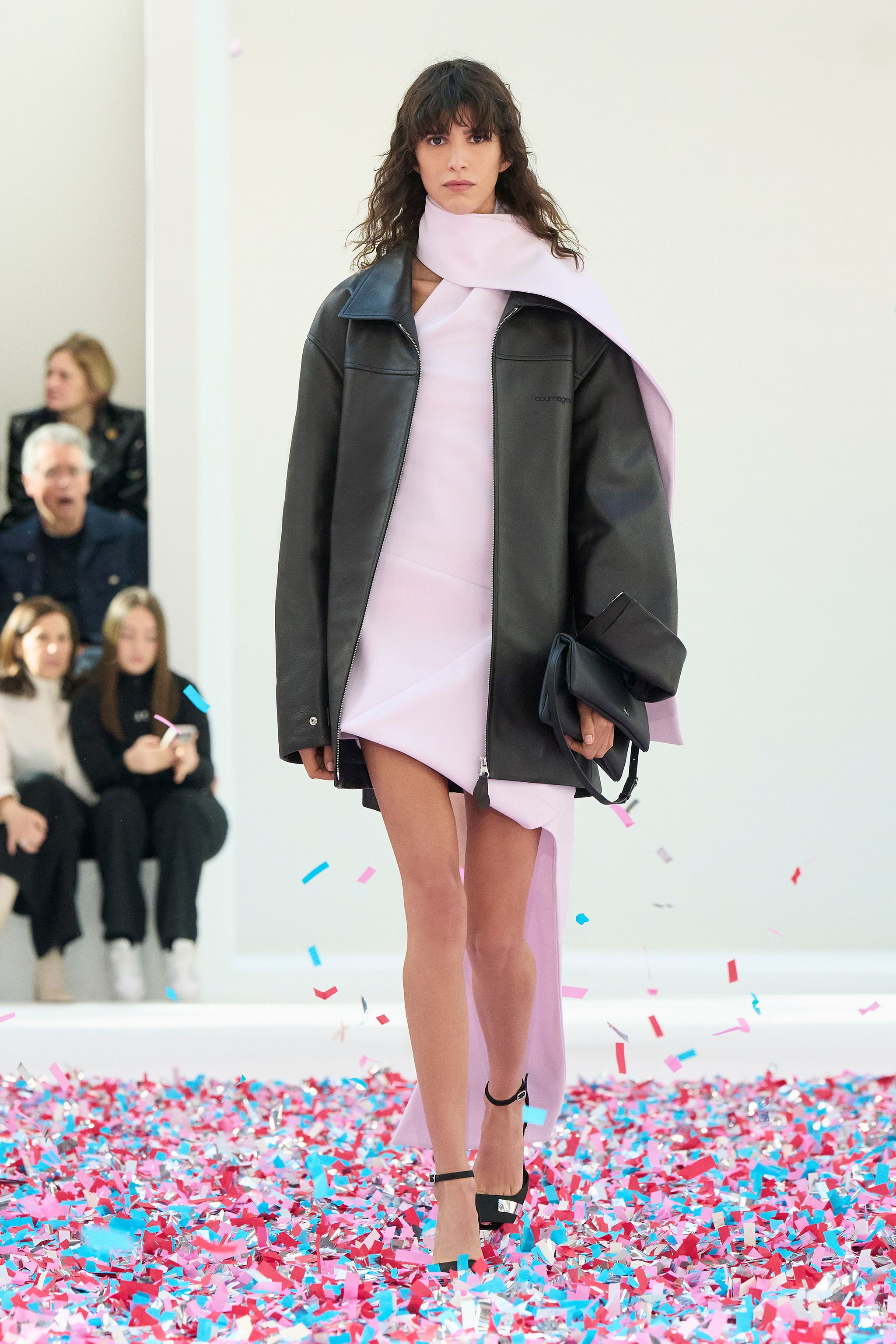 Model in pink dress and black leather jacket showcases Courrèges fashion on runway.