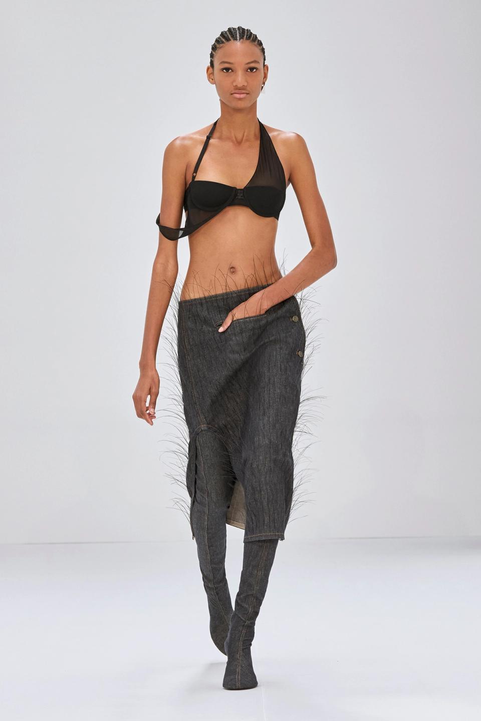 Elegant black leather dress with a faux fur stole, styled for Courrèges fashion on a runway.