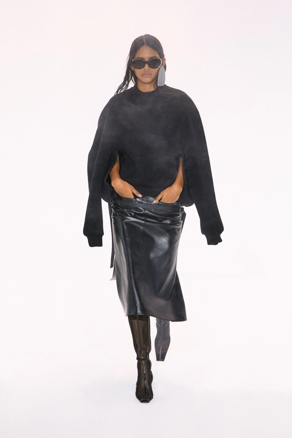 Elegant model walking in black leather skirt and oversized sweater, Courrèges fashion runway.