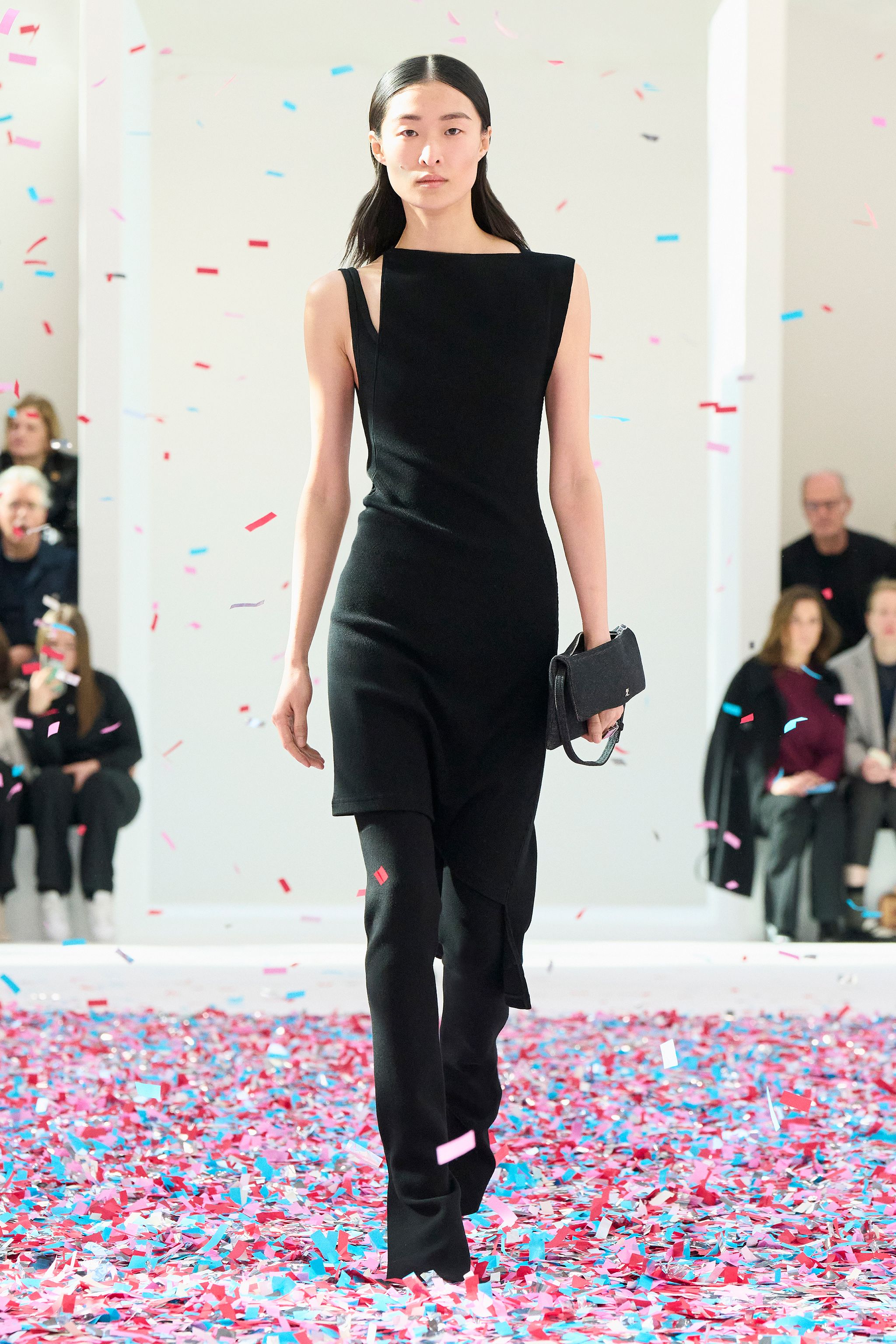 Elegant black dress walking on a runway with colorful confetti for Courrèges fashion show.