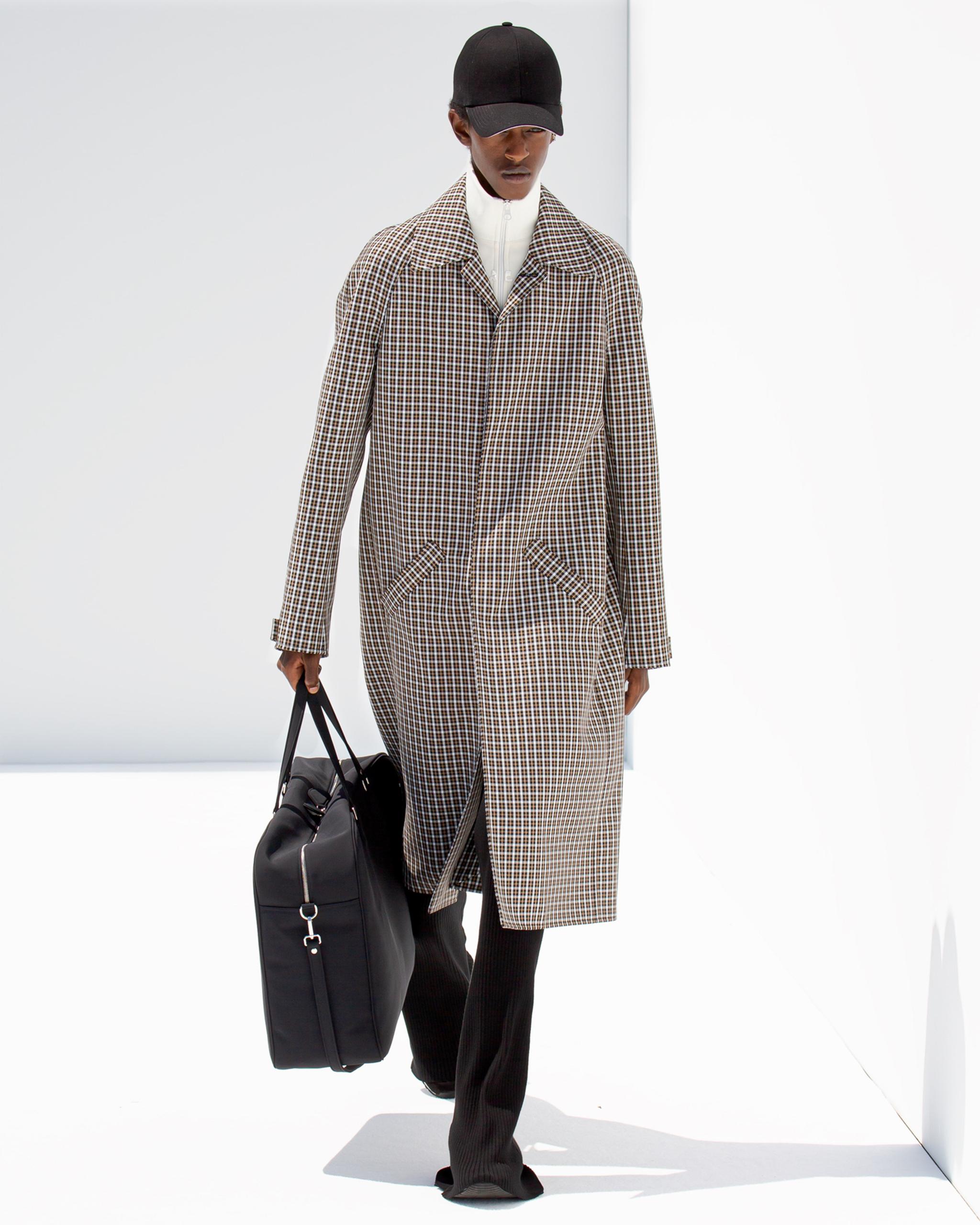 Elegant fashion look featuring Courrèges with a checkered coat, black cap, and travel bag.