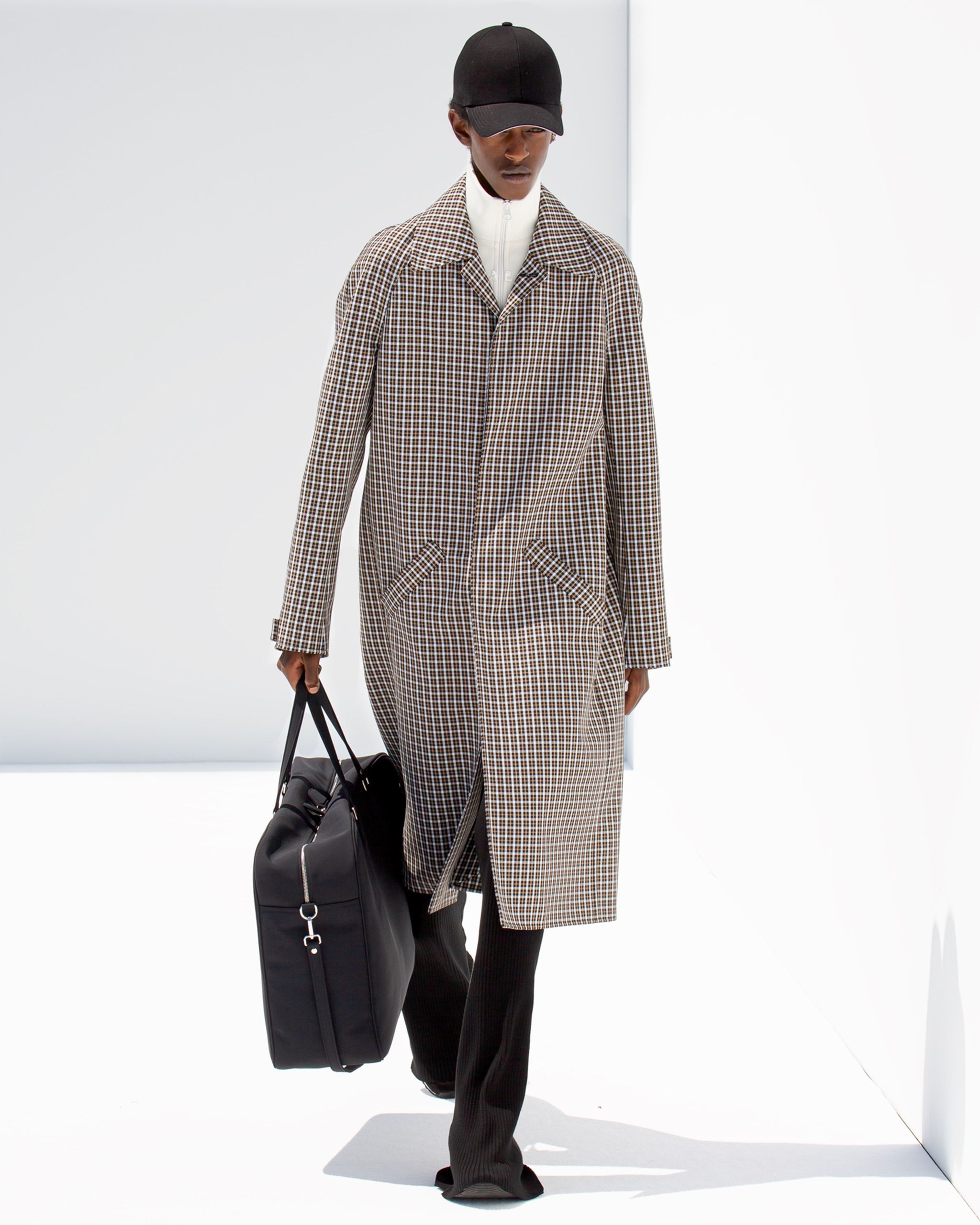 Elegant fashion look featuring Courrèges with a checkered coat, black cap, and travel bag.