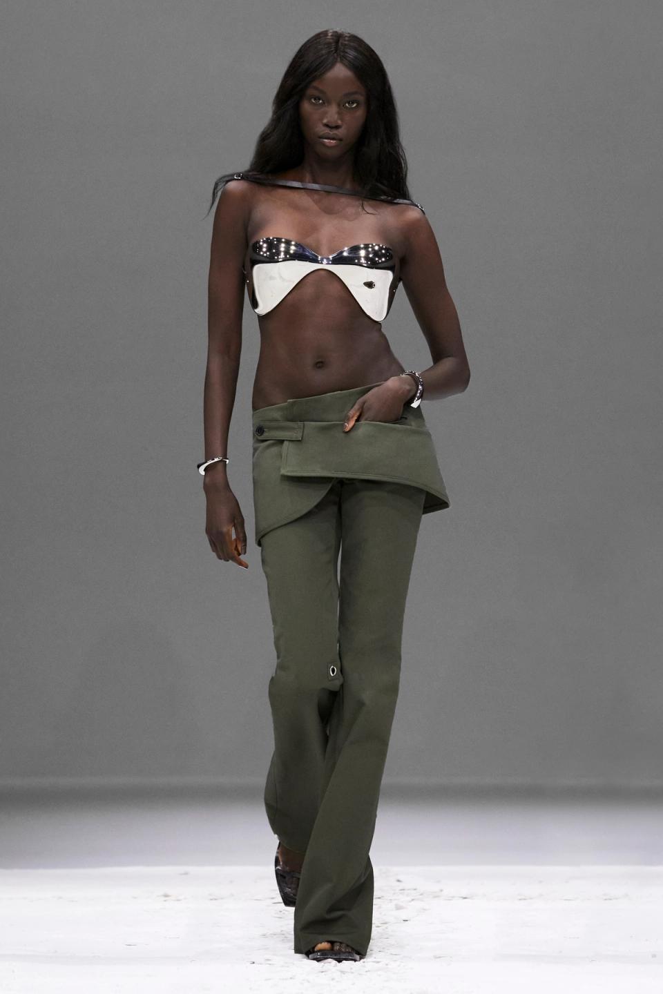 Elegant black model wearing futuristic metallic crop top and olive green pants for Courrèges.