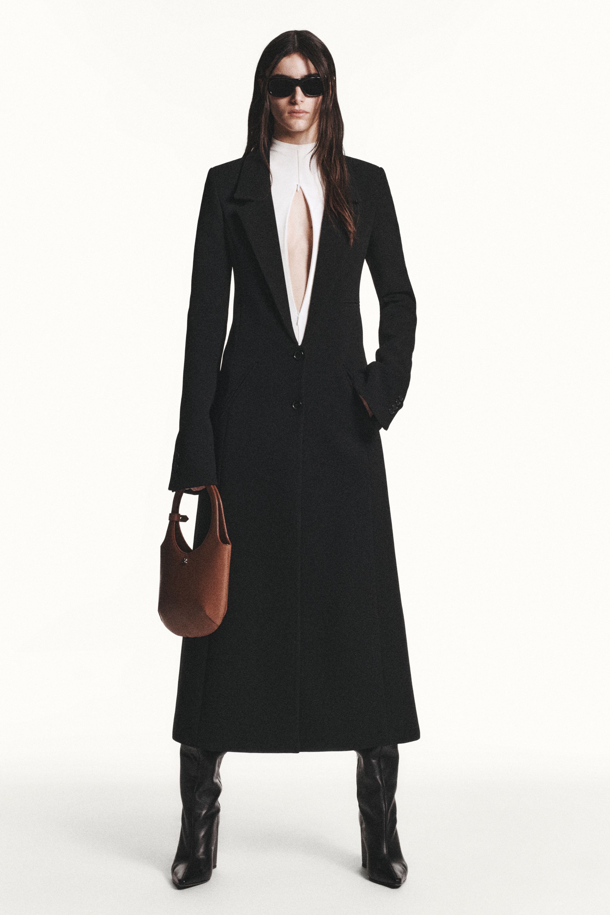 Elegant black blazer with a daring slit, paired with sheer tights, sunglasses, and high heels for Courrèges.