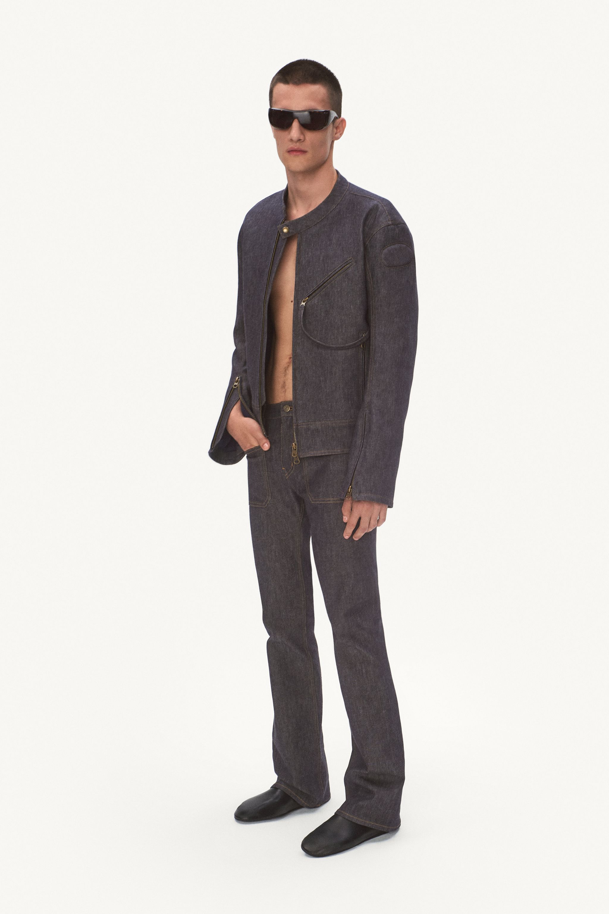 Elegant male fashion model in dark denim jacket and jeans, wearing stylish sunglasses for Courrèges.