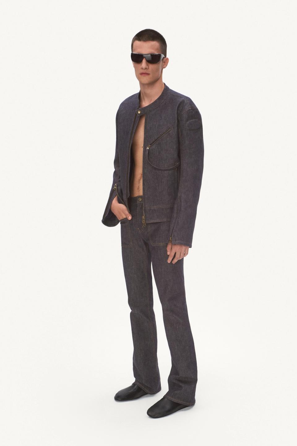 Elegant male fashion model in dark denim jacket and jeans, wearing stylish sunglasses for Courrèges.