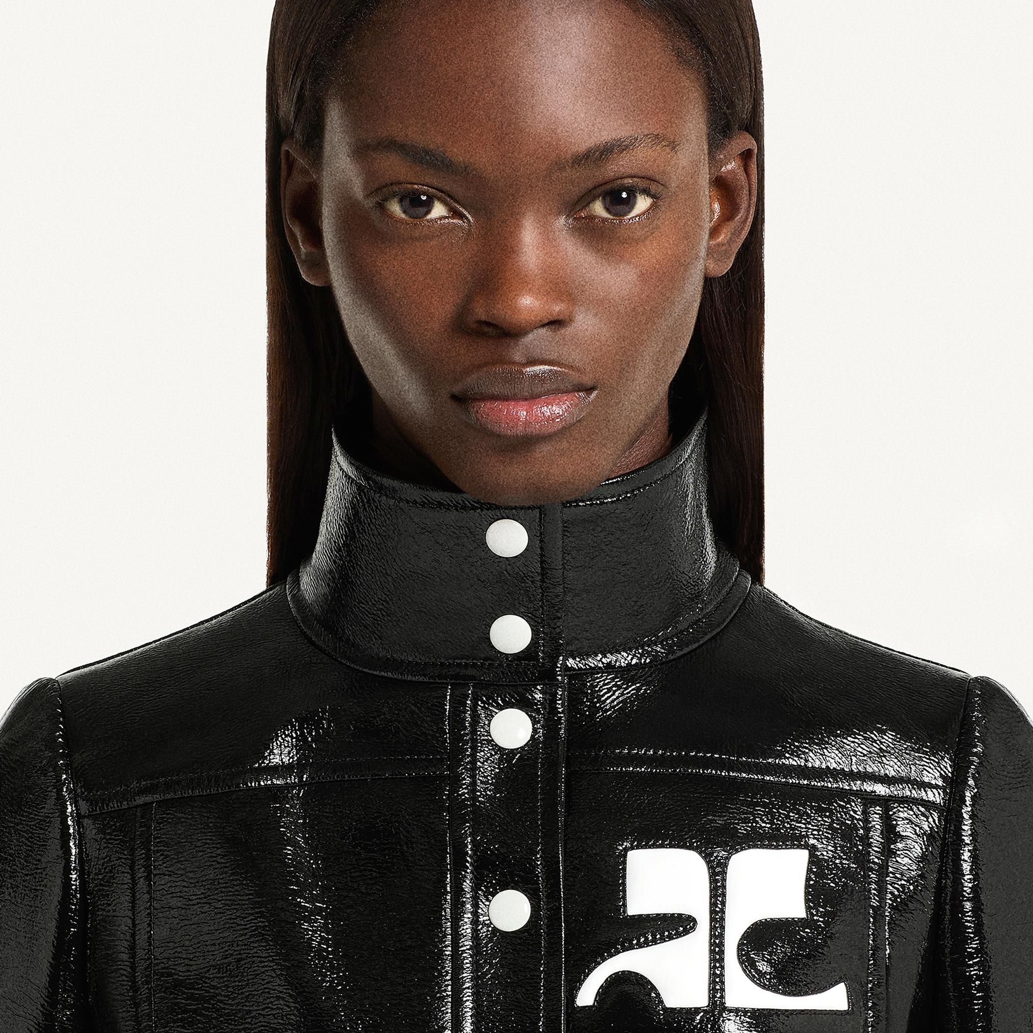 Elegant close-up of a model wearing a glossy black leather Courrèges jacket with white logo details.