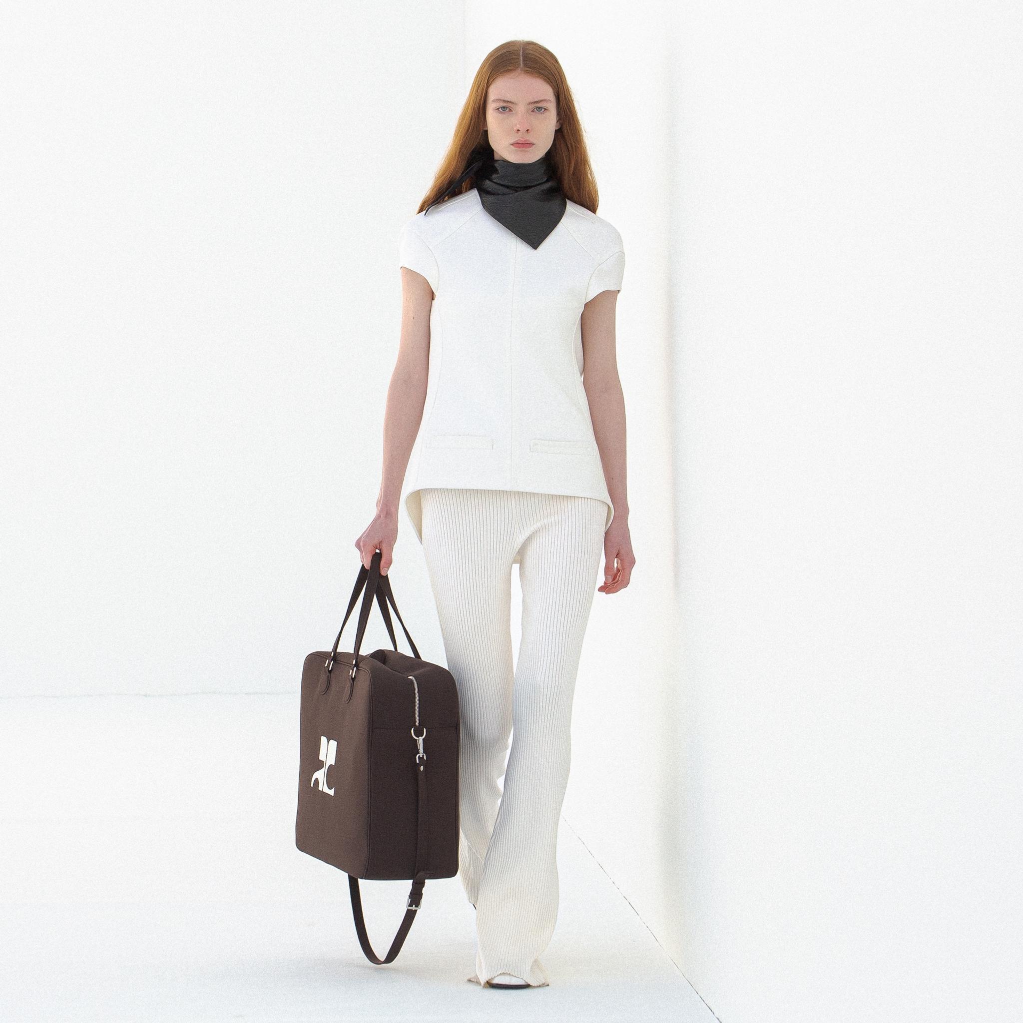 Modèle élégant de Courrèges en tenue blanche avec accessoires noirs sur un fond minimaliste