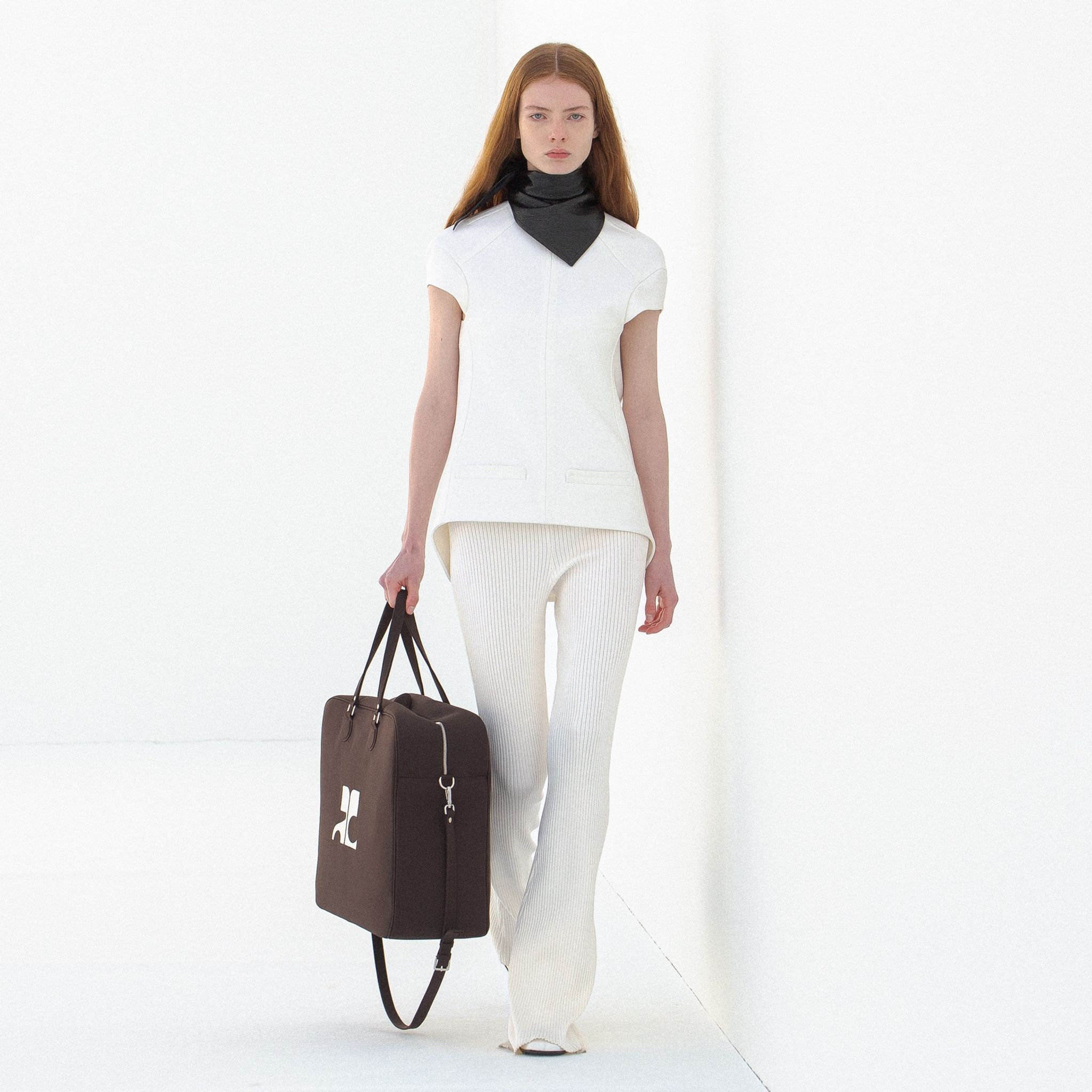 Elegant Courrèges fashion model in white outfit with black accessories on a minimalist runwa