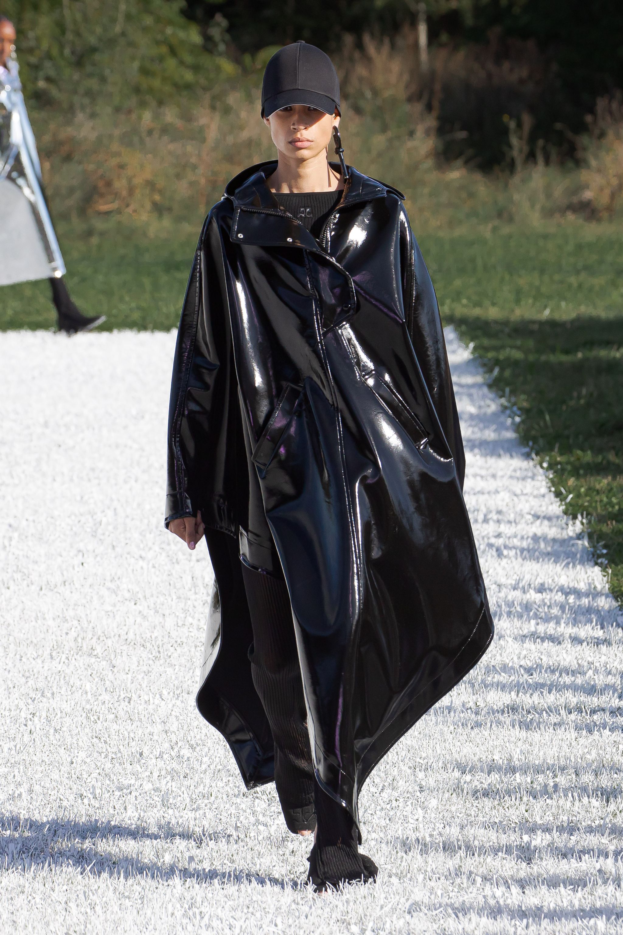 Elegant black shiny raincoat by Courrèges on a fashion runway, perfect for modern style.
