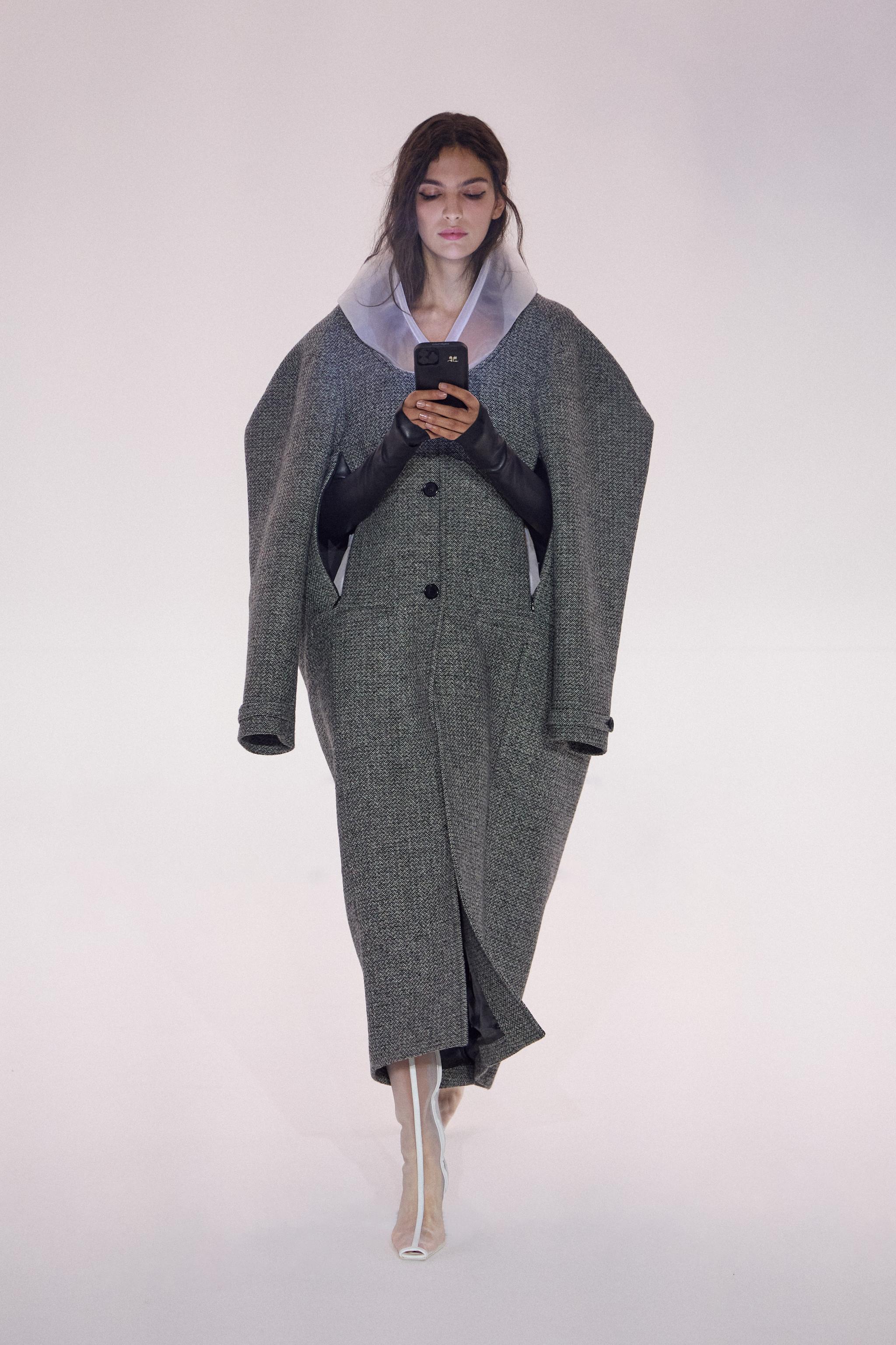 Elegant model in a grey coat and gloves, showcasing Courrèges fashion on a runway.